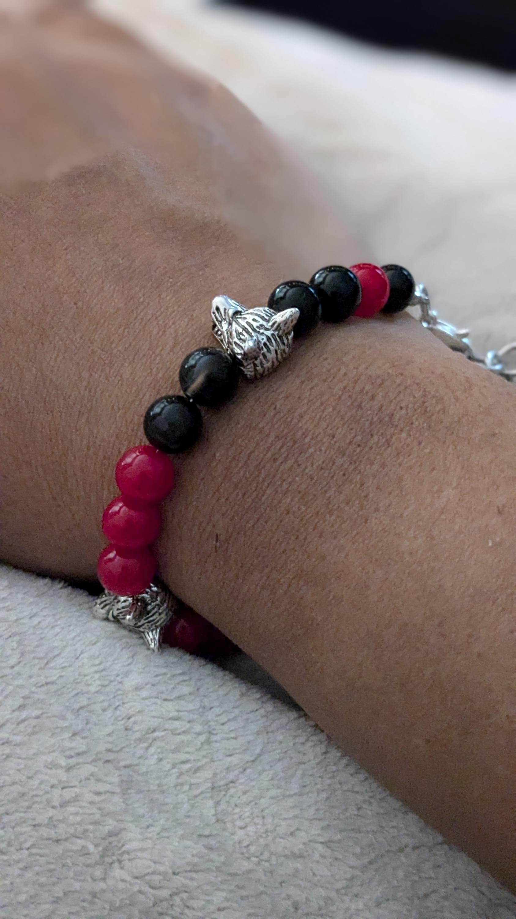 A close-up image of a person wearing a bracelet with silver wolf head shaped bead accents, black beads, and red round glass beads.