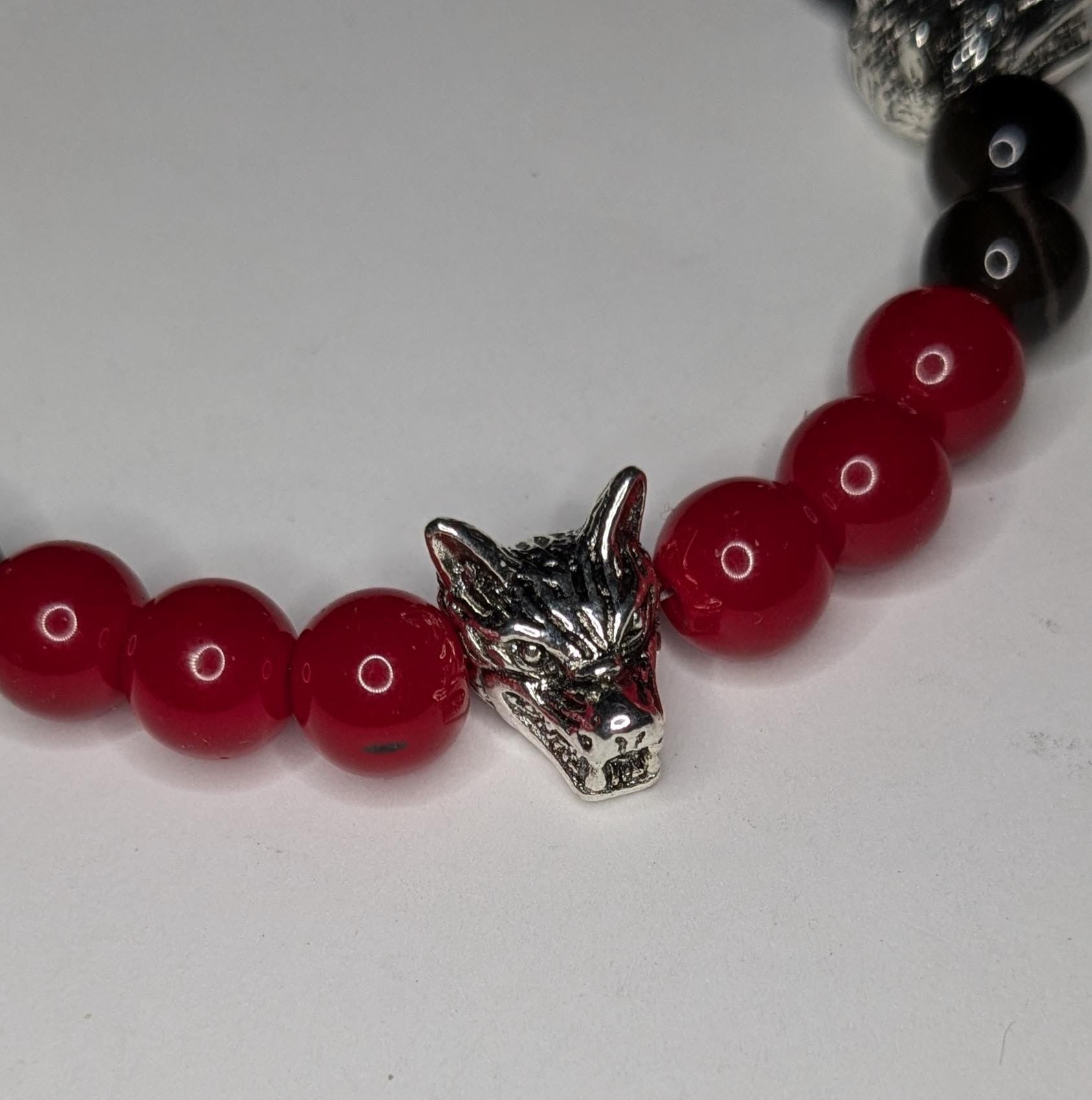 Close up of one of the silver toned wolf head beads showing the detail of the eyes, fur and teeth. This bead is between three red beads on the left and three red and two black beads on the right.