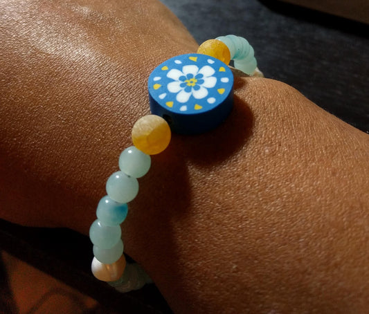 Beaded bracelet with a blue, white and yellow floral focal and blue glass and yellow agate beads on a person's wrist.