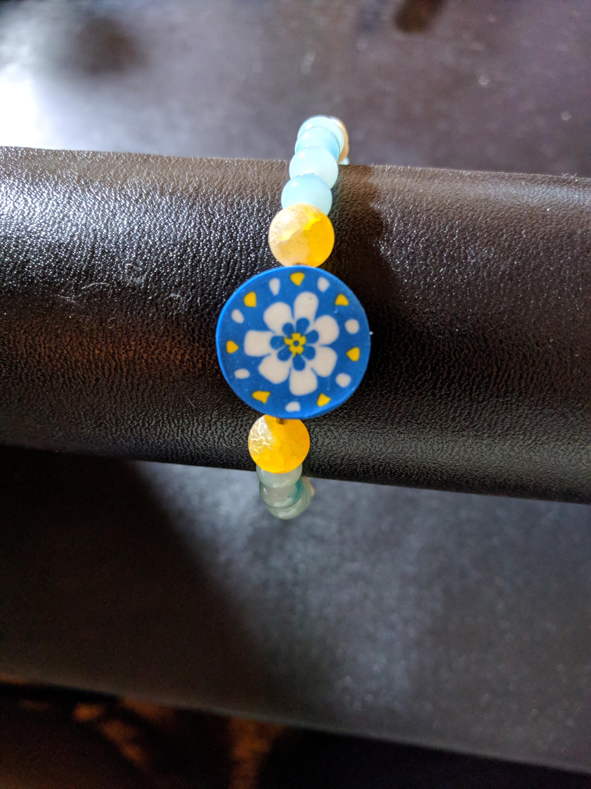 Beaded bracelet with a blue, white and yellow floral focal on a black bead display.