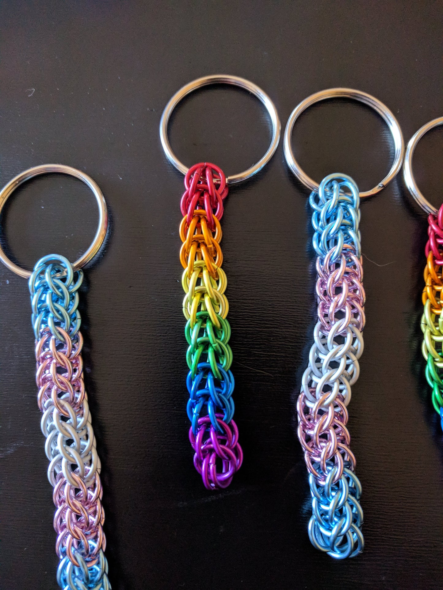 A selection of colorful chainmail keychains in pride colors with split rings, displayed on a dark background.