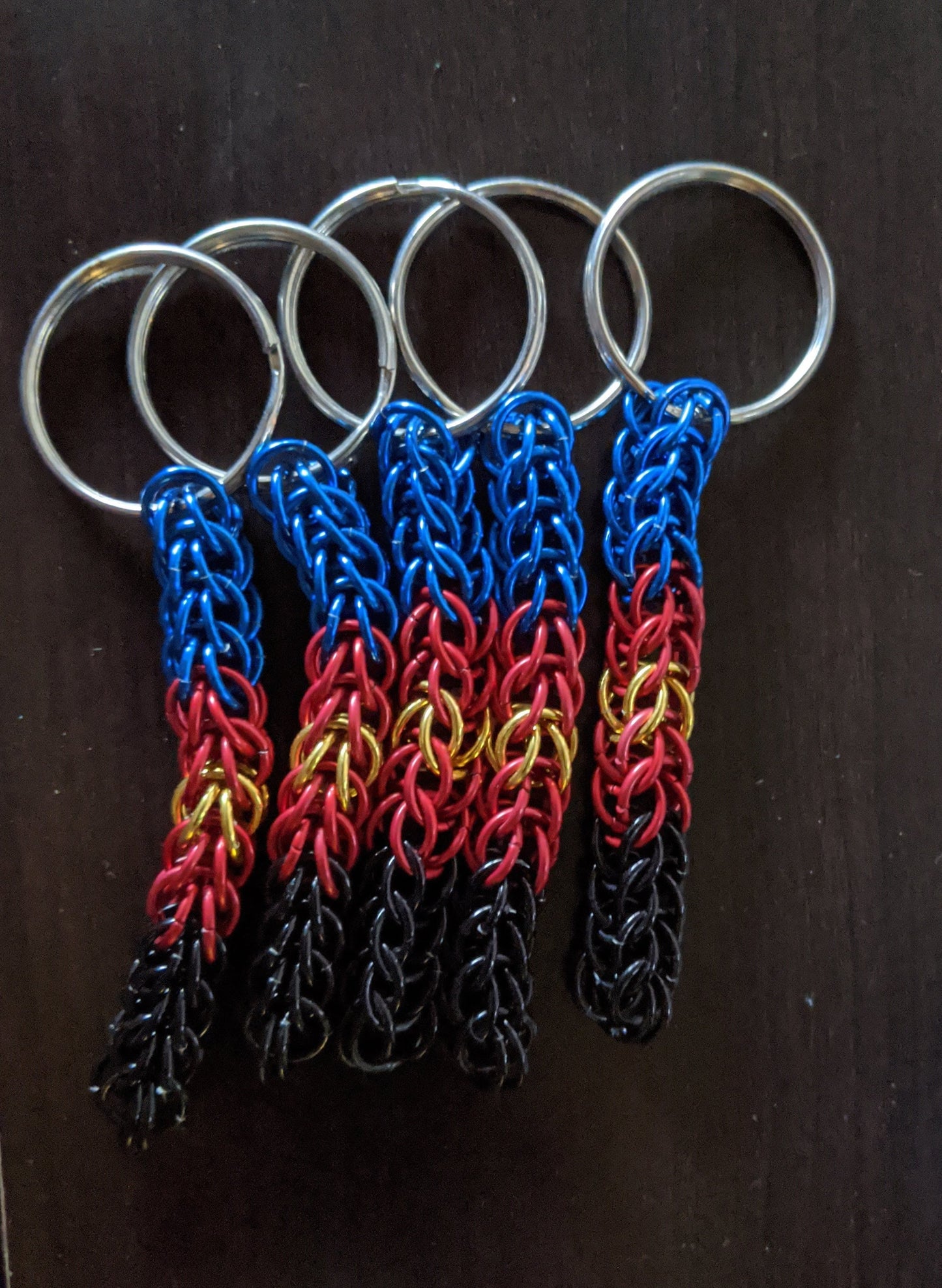 5 chainmail keychains in polyam pride colors on a dark background