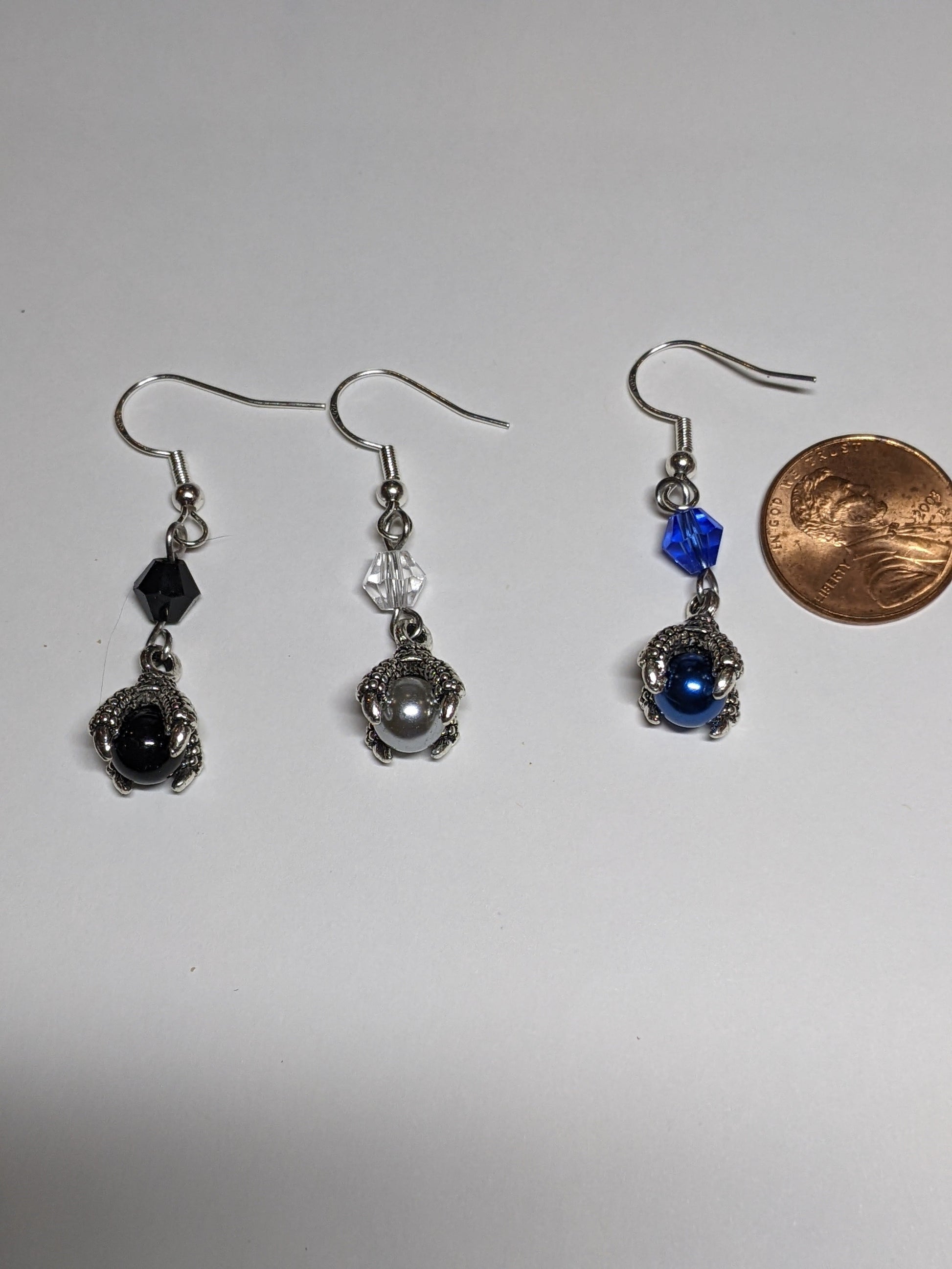3 dragon claw earrings with pearls, displayed next to a coin for scale.