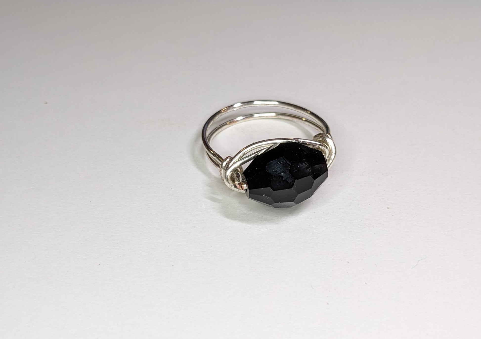 Close up for wire wrapped faceted glass ring on a white background. Ring points slightly to the right.