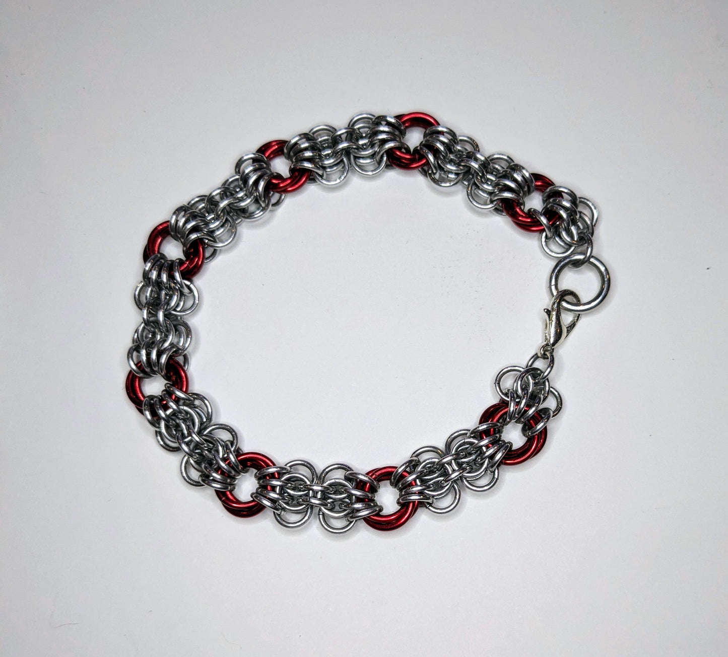 Silver and red butterfly weave chainmail bracelet on a white background. Bracelet has a lobster clasp.