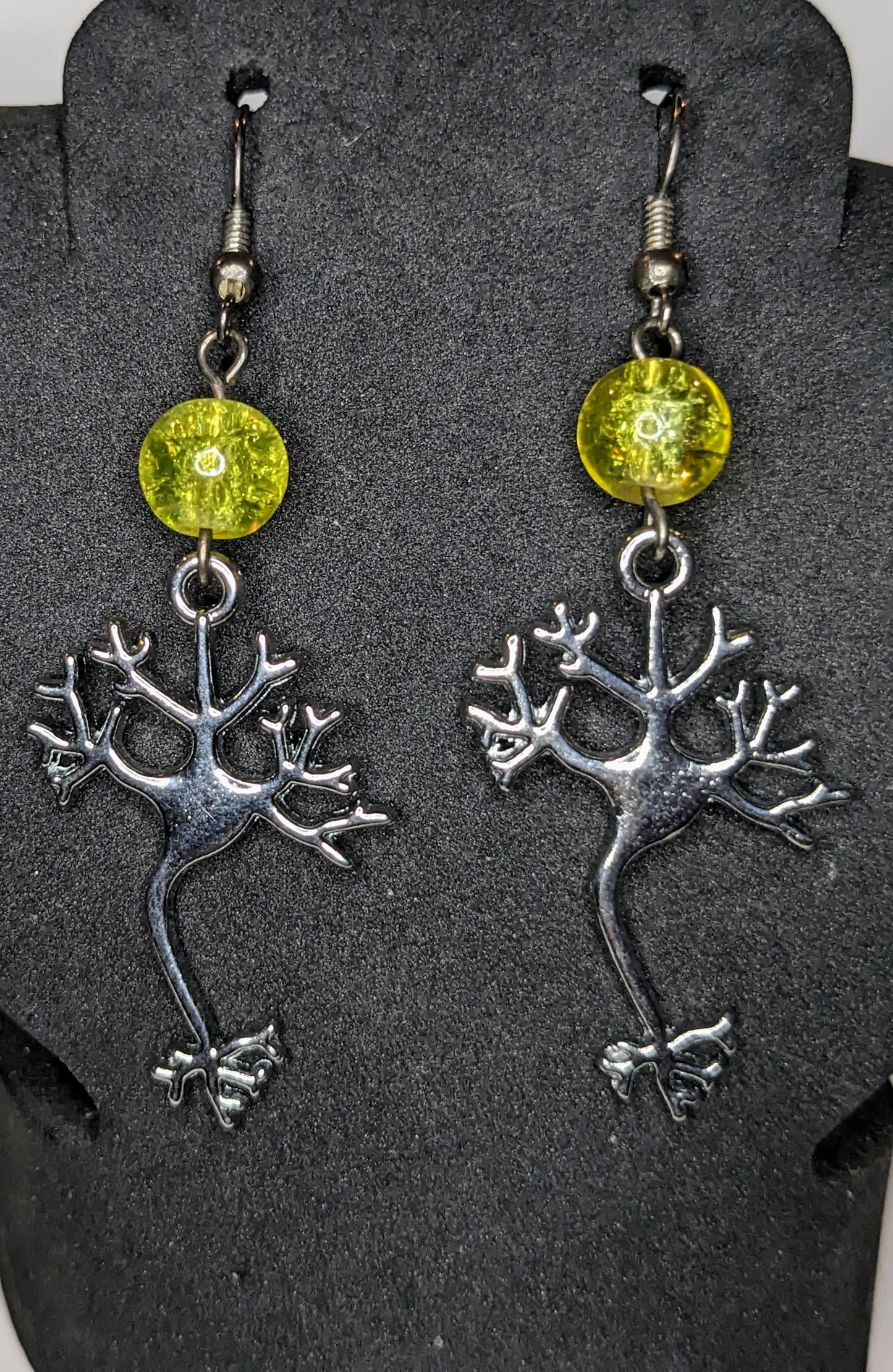Earrings on a black display. Earrings are silver neuron charms with a yellow glass crackle bead