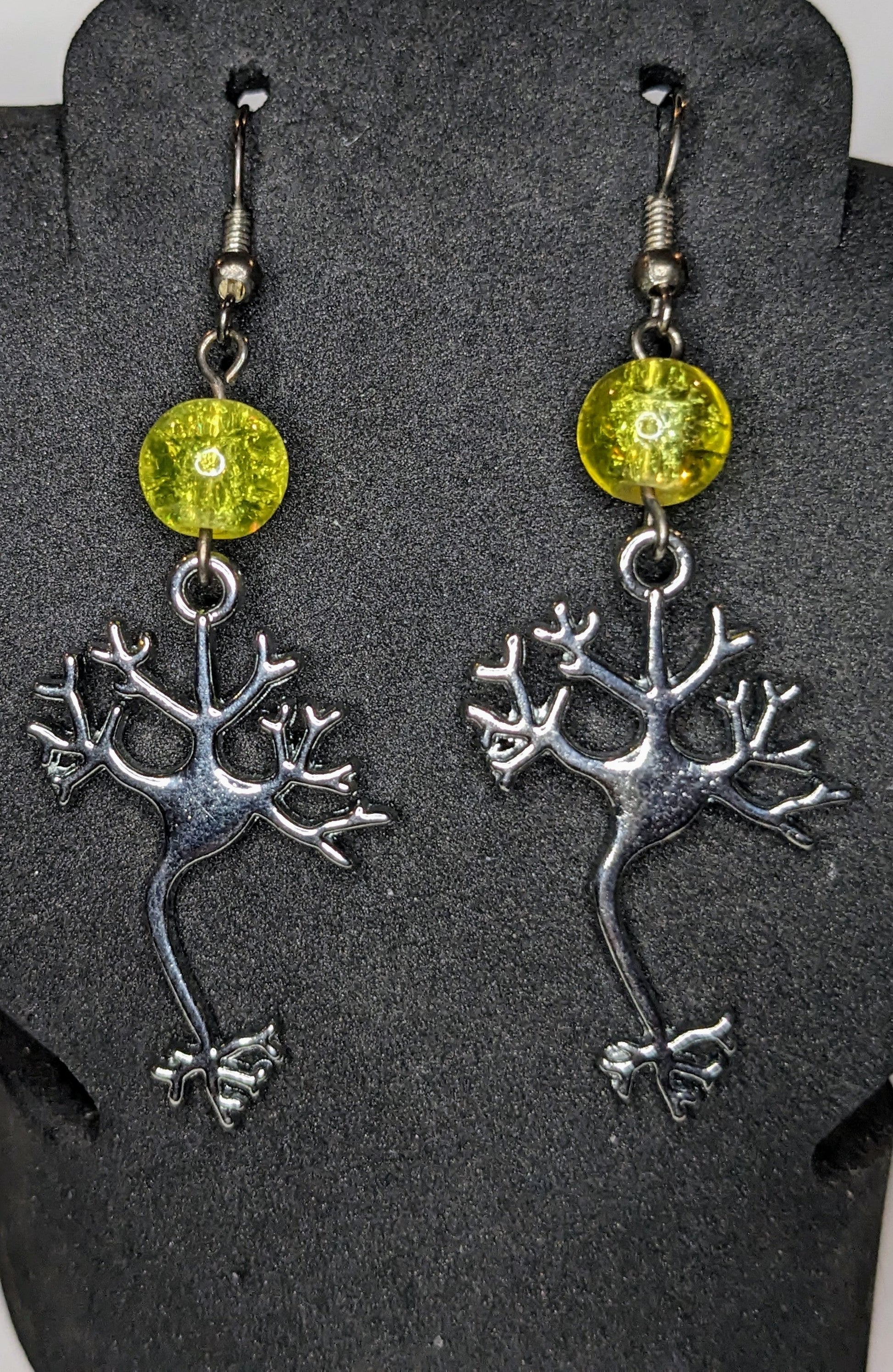 Earrings on a black display.  Earrings are silver neuron charms with a yellow glass crackle bead accent