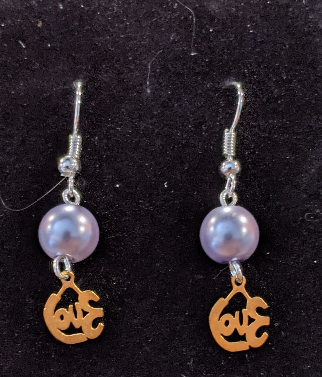 A pair of drop earrings featuring gold-colored cut-out charms that say love and pearl beads.