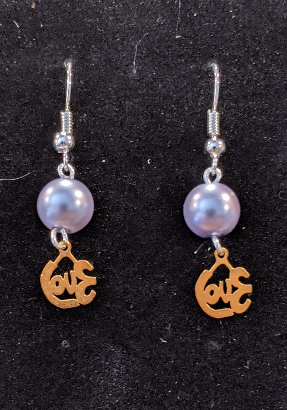 A pair of drop earrings featuring gold-colored cut-out charms that say love and pearl beads.