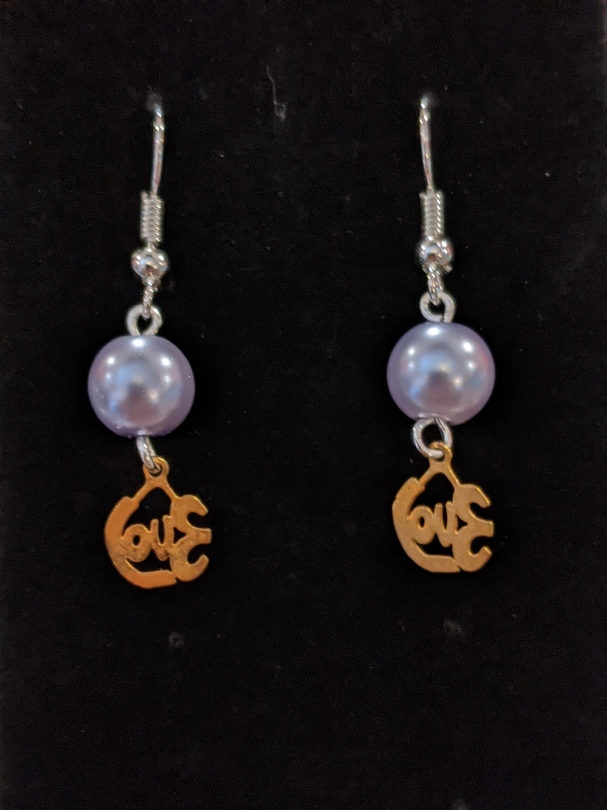 A pair of drop earrings featuring gold-colored cut-out charms that say love and pearl beads.