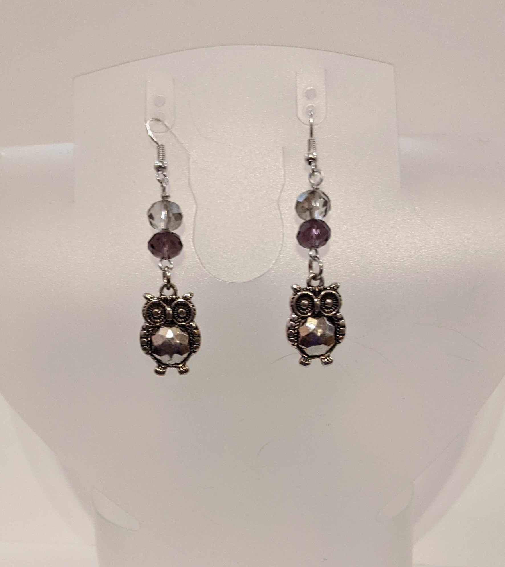 A pair of silver-plated owl earrings with faceted glass beads in gray and purple hues.
