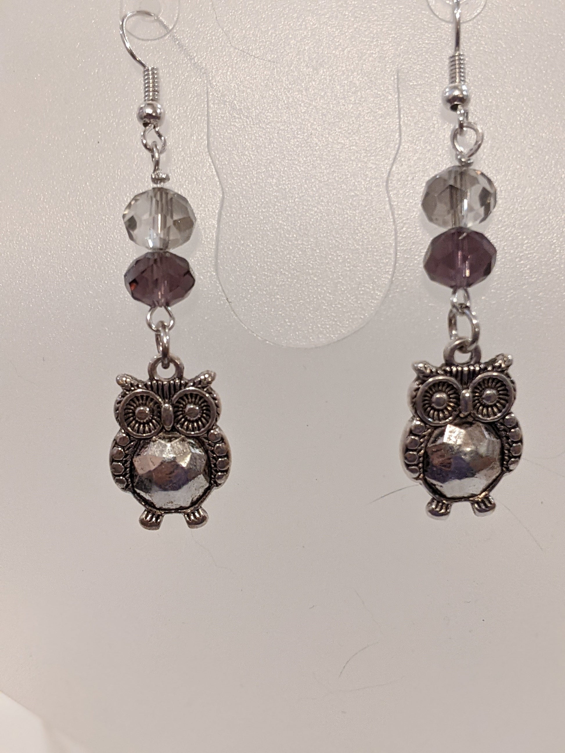 A pair of silver-plated owl earrings with faceted glass beads in gray and purple hues.