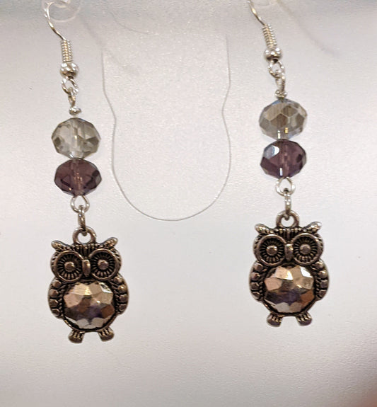 A pair of silver-plated owl earrings with faceted glass beads in gray and purple hues.
