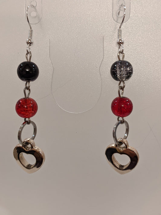A pair of dangle earrings featuring black and red glass crackle beads with silver heart charms, dangling from silver-toned wires.