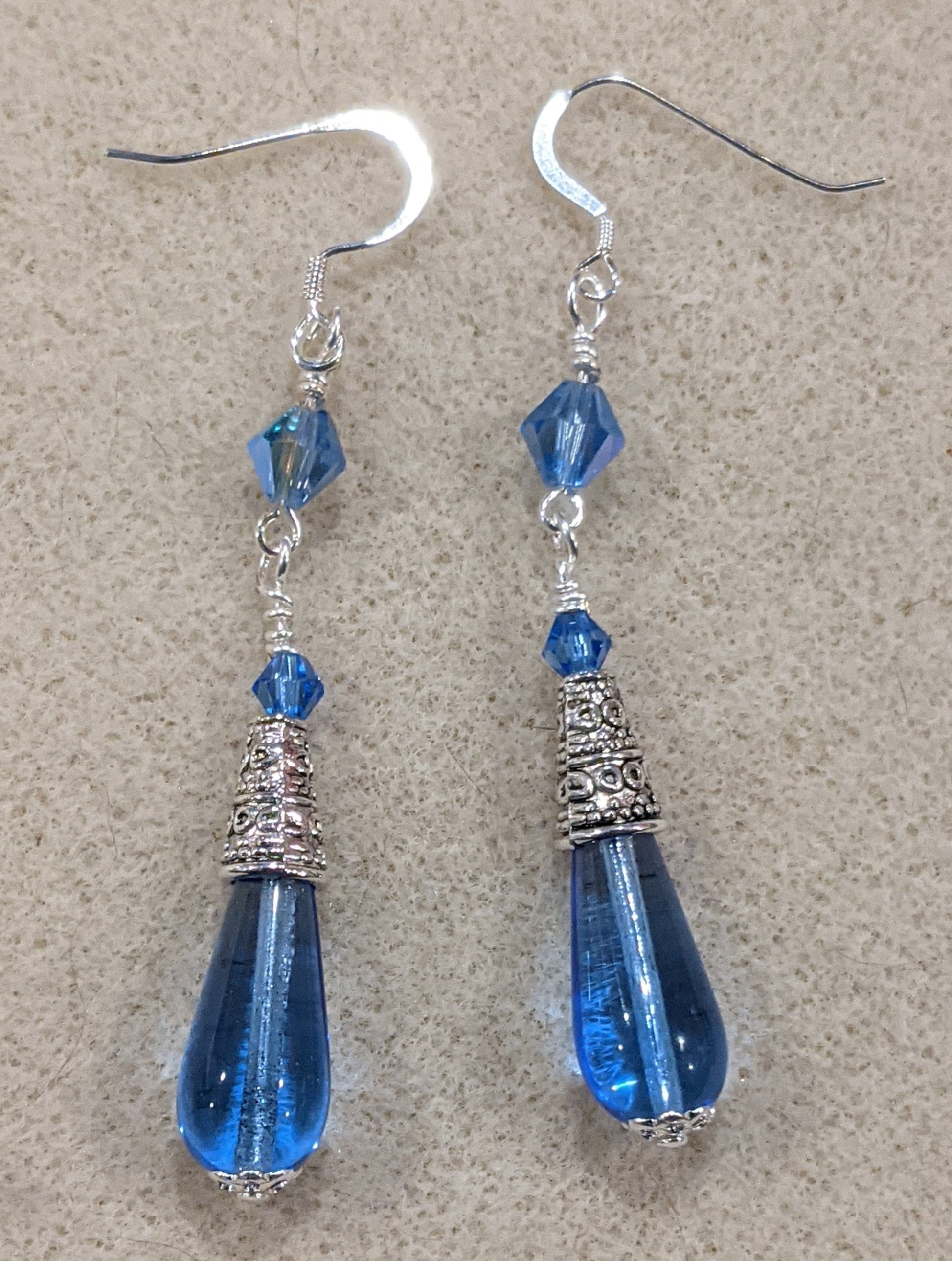 Blue Czech pressed glass teardrop dangle earrings with crystal accents on an off-white textured background