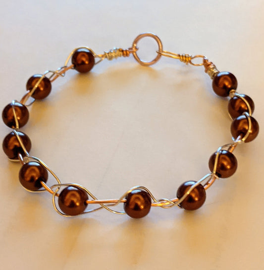 A bracelet with brown glass pearls and silver wire wrapped around them, featuring a hook and eye closure.