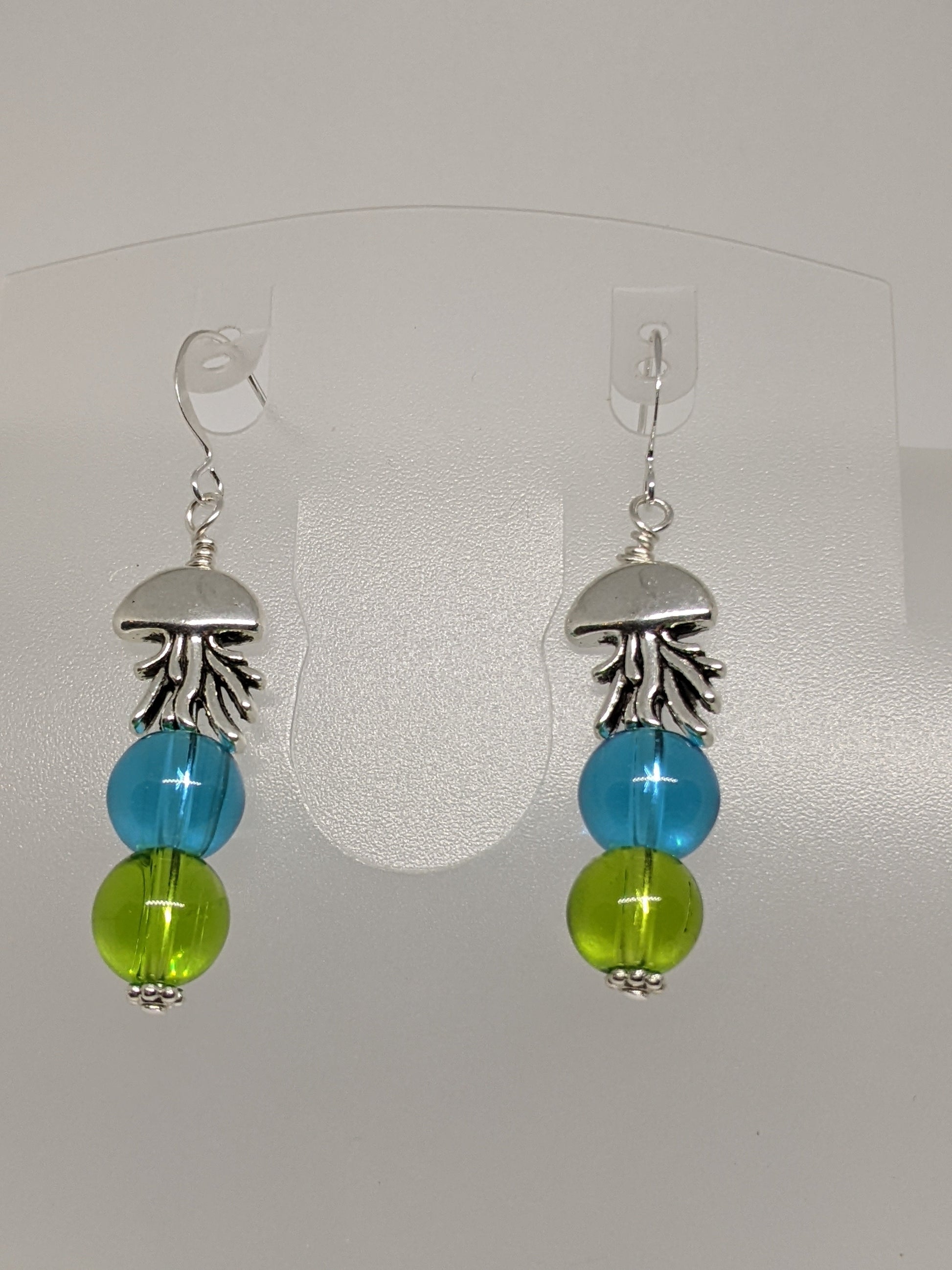 A pair of earrings featuring silver jellyfish shapes with clear blue and green round glass beads attached to silver plated ear wires.