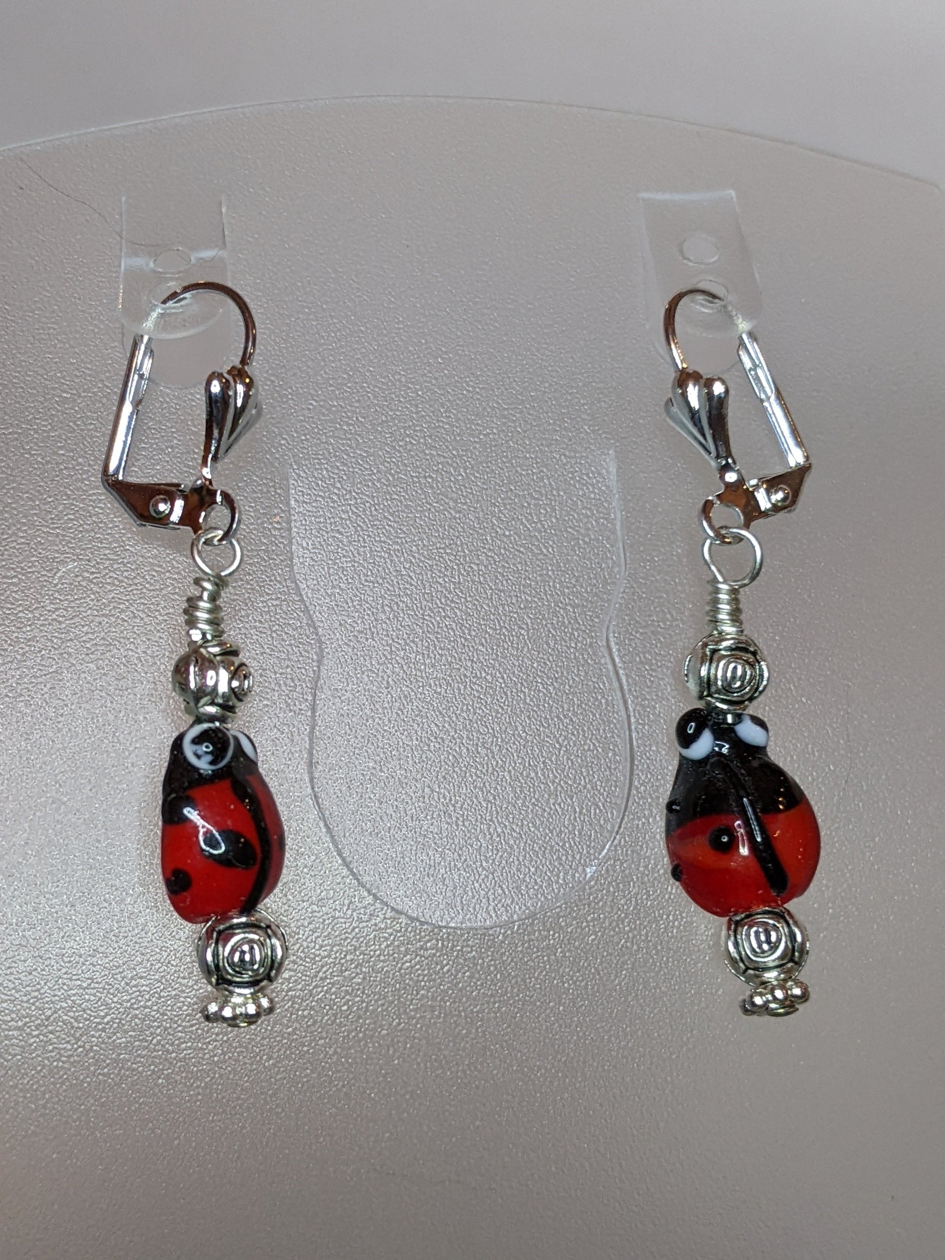 A pair of earrings featuring lamp work ladybug beads, silver rosebuds, and silver plated lever back ear wires.