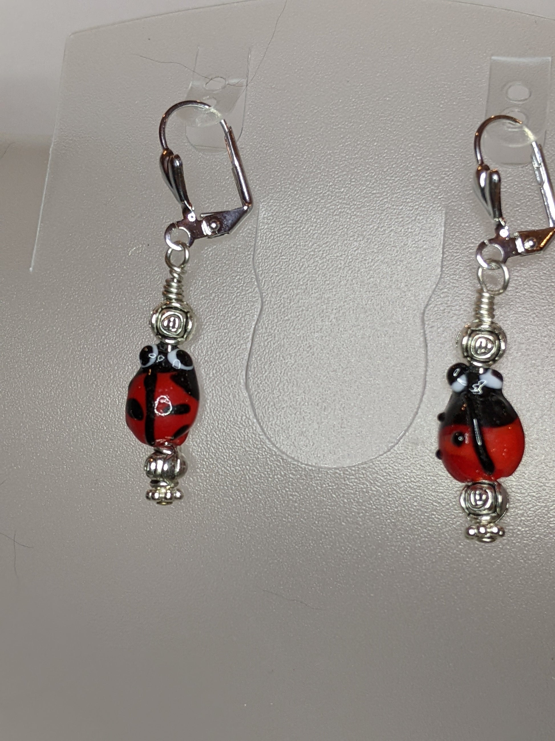 A pair of earrings featuring lamp work ladybug beads, silver rosebuds, and silver plated lever back ear wires.