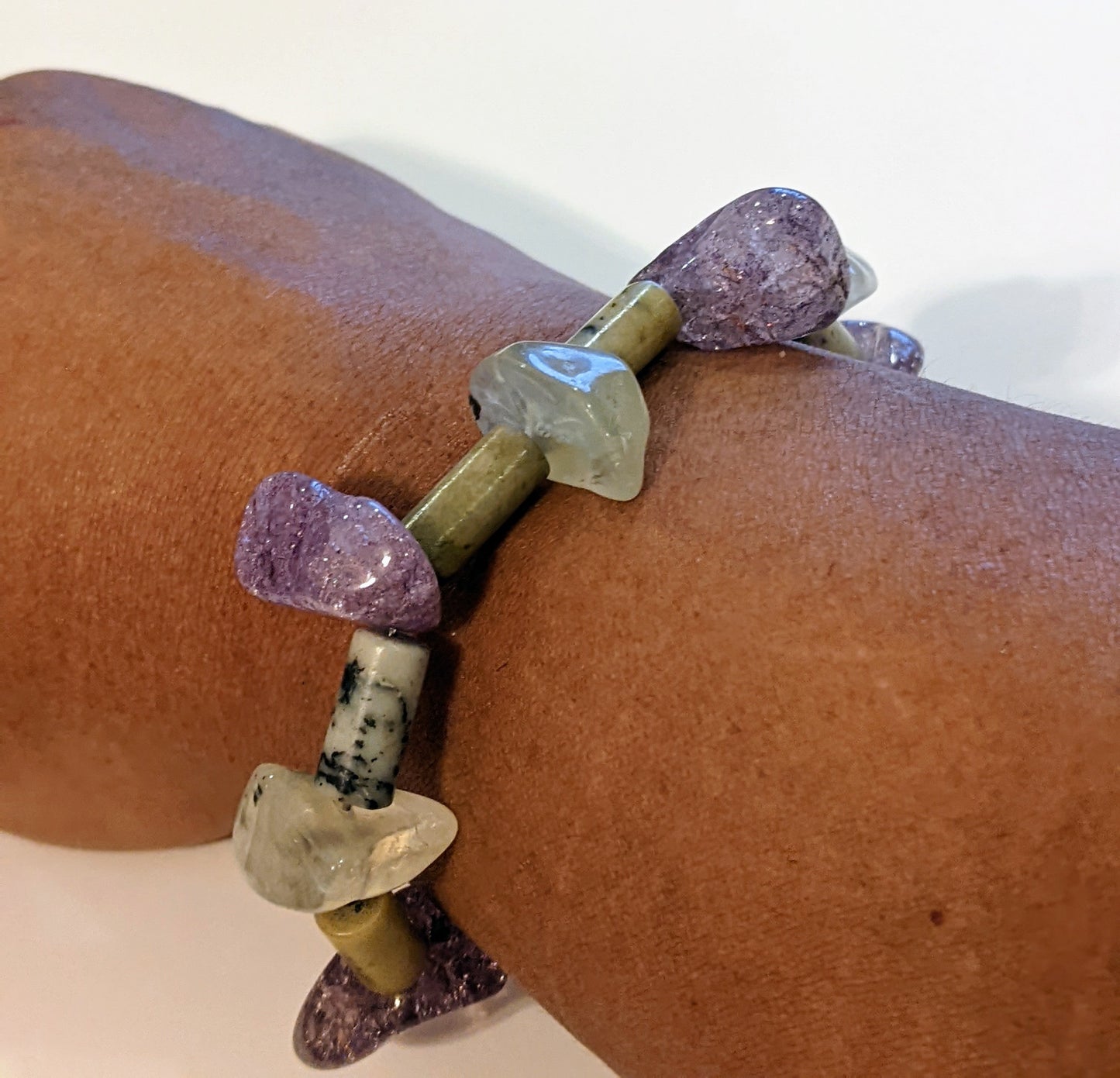 Beaded bracelet on brown person's wrist. Bracelet is crafted from amethyst and green aventurine nuggets with stone tube beads between.