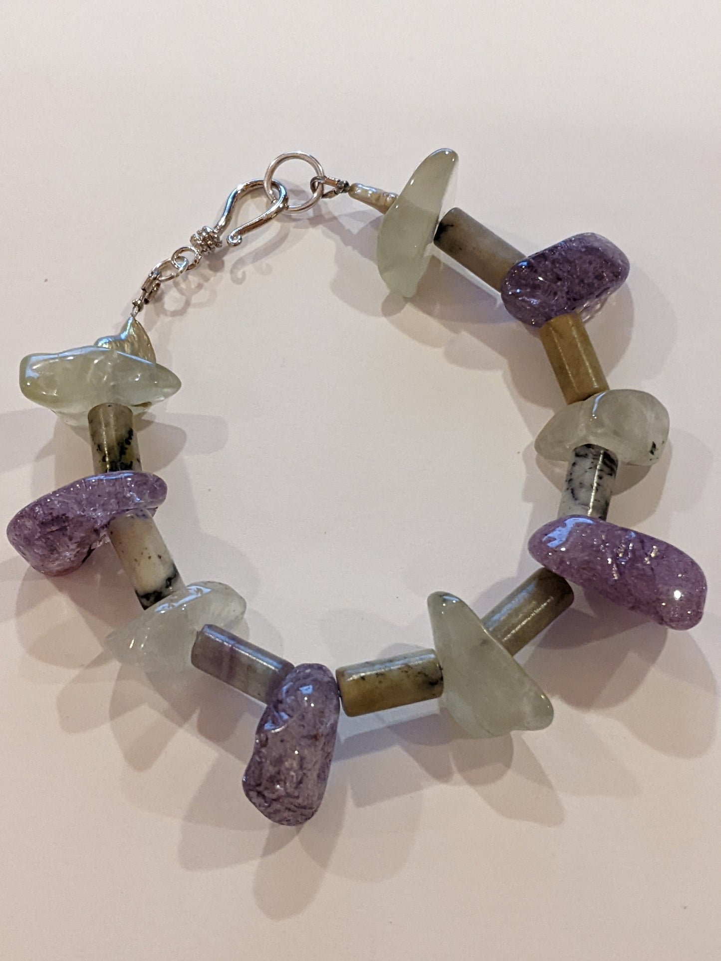 Beaded bracelet on white background. Bracelet is crafted from amethyst and green aventurine nuggets with stone tube beads between. Bracelet has a silver hook & eye clasp.