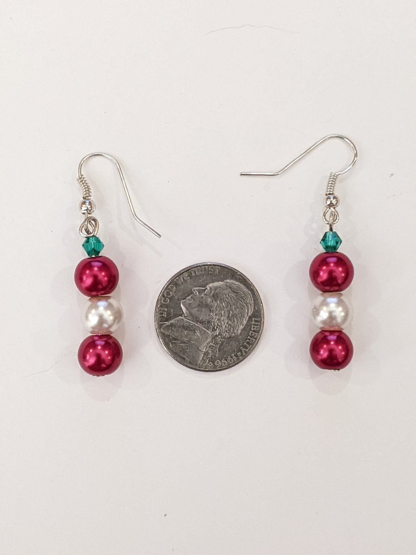 A pair of pearl bead dangle earrings with red and white glass pearls and green faceted bicone, on silver French hook ear wires with a nickel between showing size.