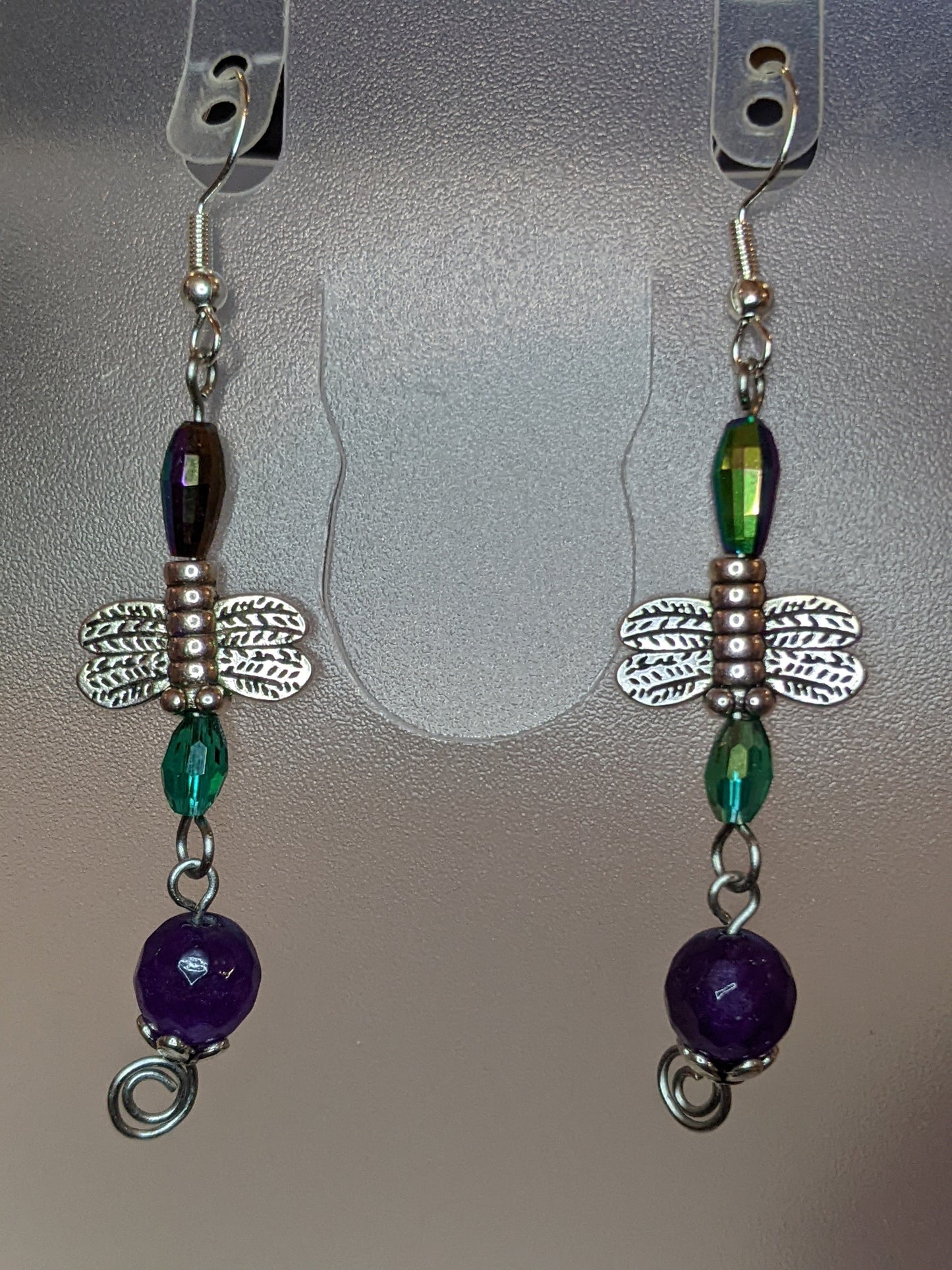 A pair of beaded dangle earrings featuring purple and green beads with silver-colored dragonfly charms.