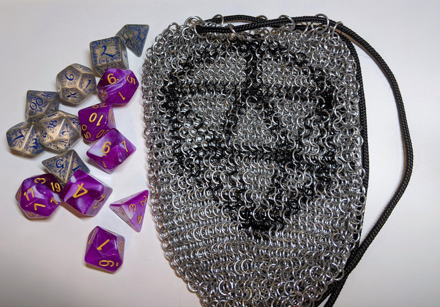 Silver chainmail dice bag with a black D20 outline next to two sets of dice, one pink and sparkly and the other clear and spooky