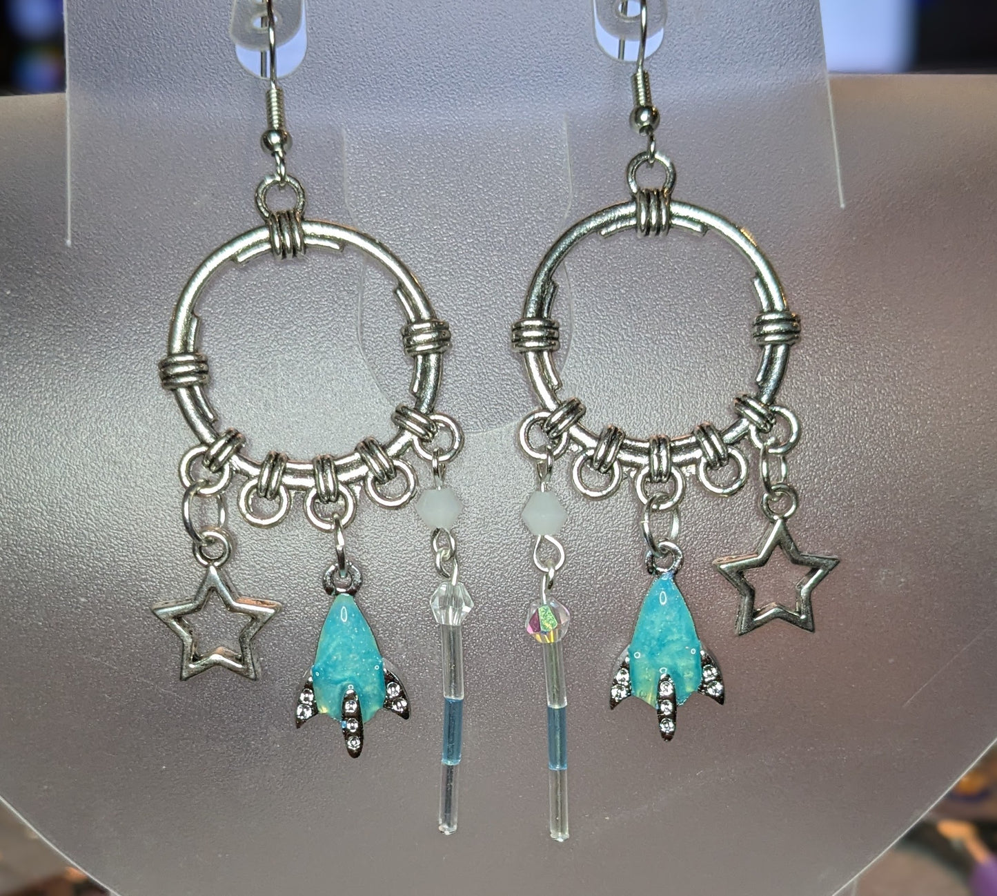 Pair of silver hoop earrings with star and turquoise charm on a gray background