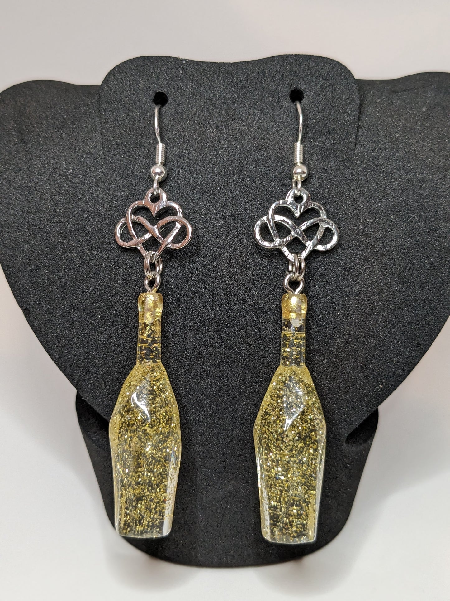 Golden faceted potion bottle earrings with silver infinity heart charms on a dark grey display stand