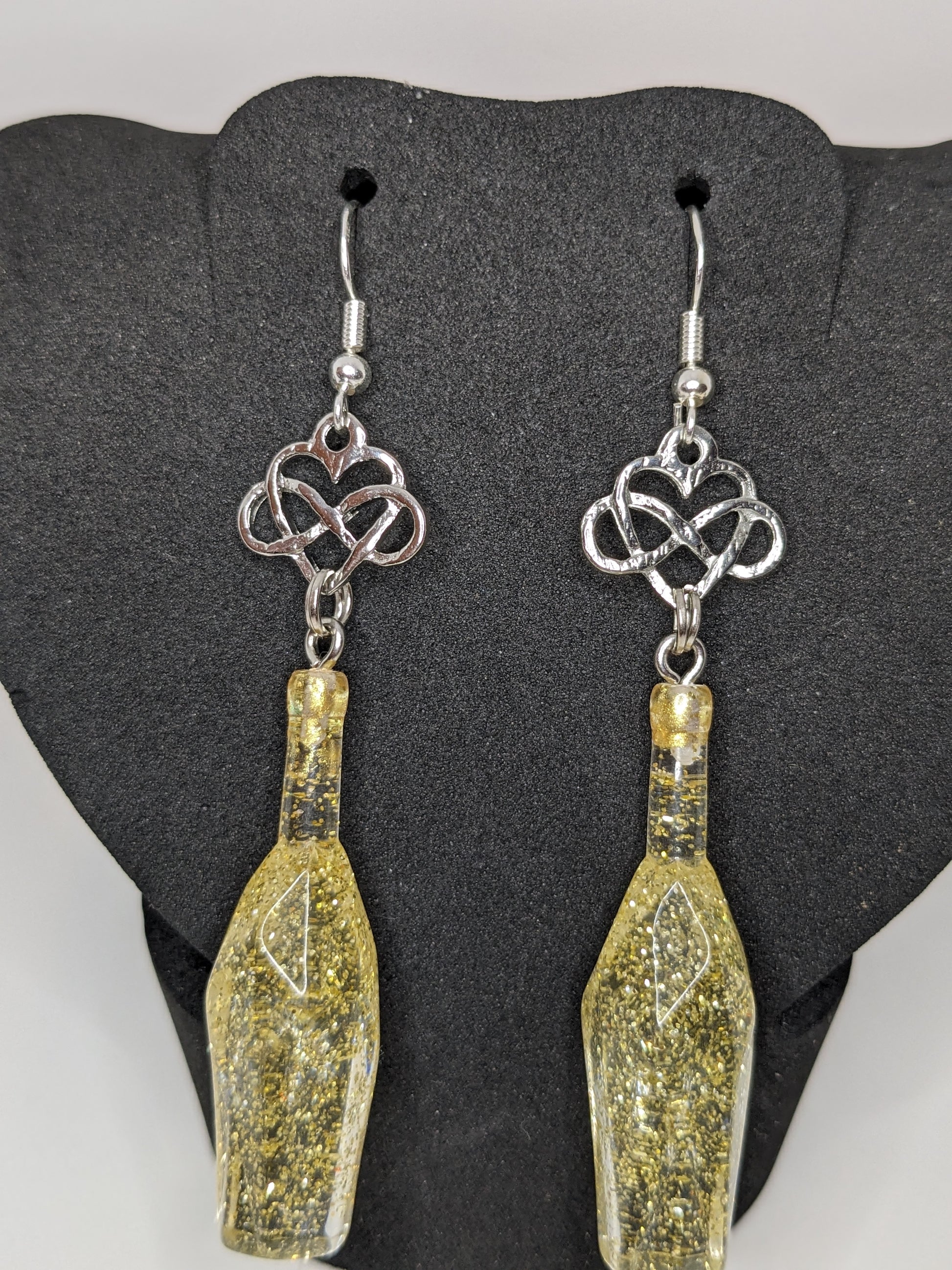 Golden faceted potion bottle earrings with silver infinity heart charms on a dark grey display stand