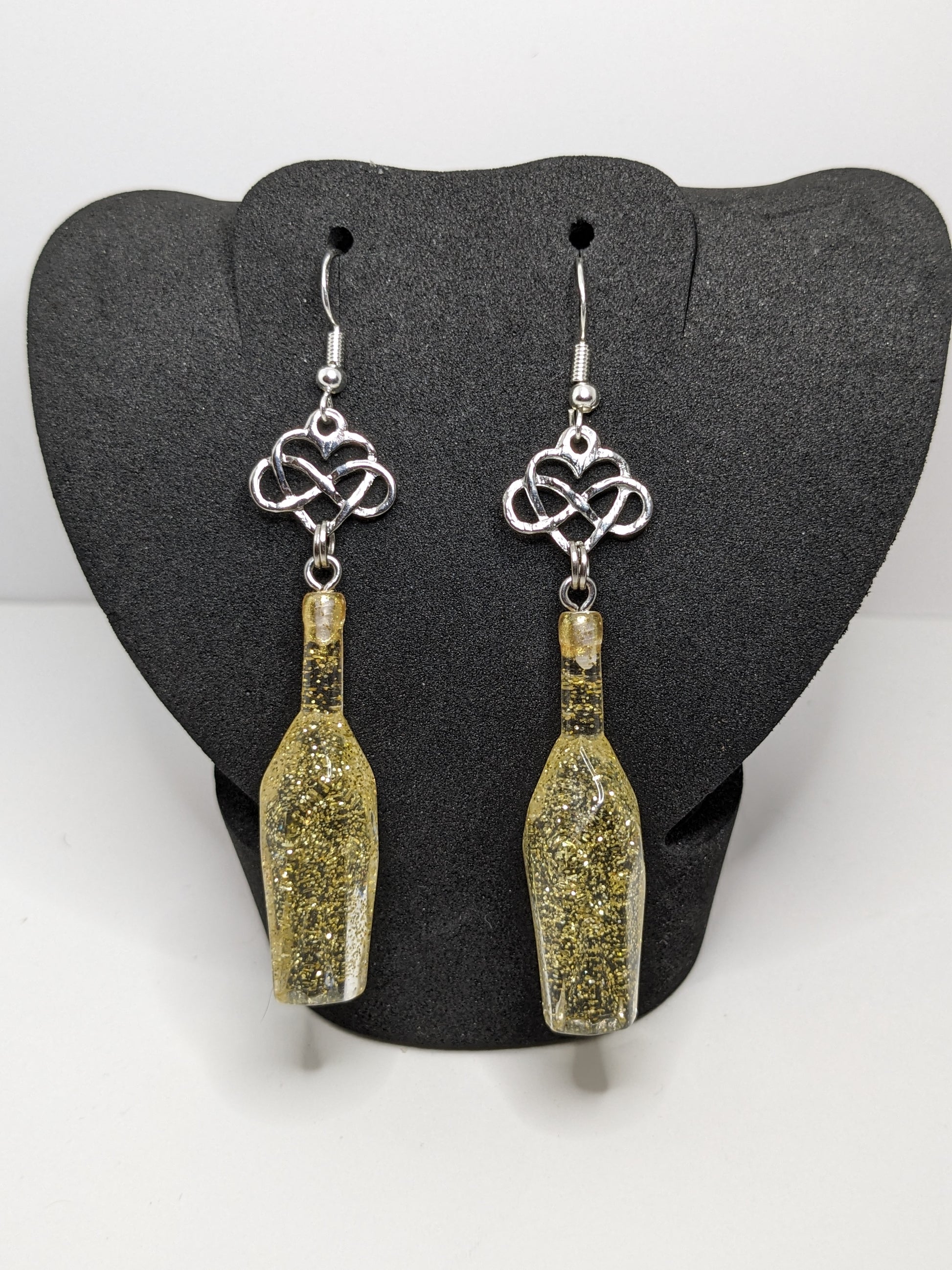Golden faceted potion bottle earrings with silver infinity heart charms on a dark grey display stand