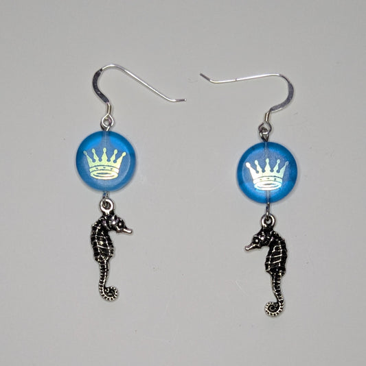 Pair of earrings with blue circular charms and seahorse pendants on a gray background
