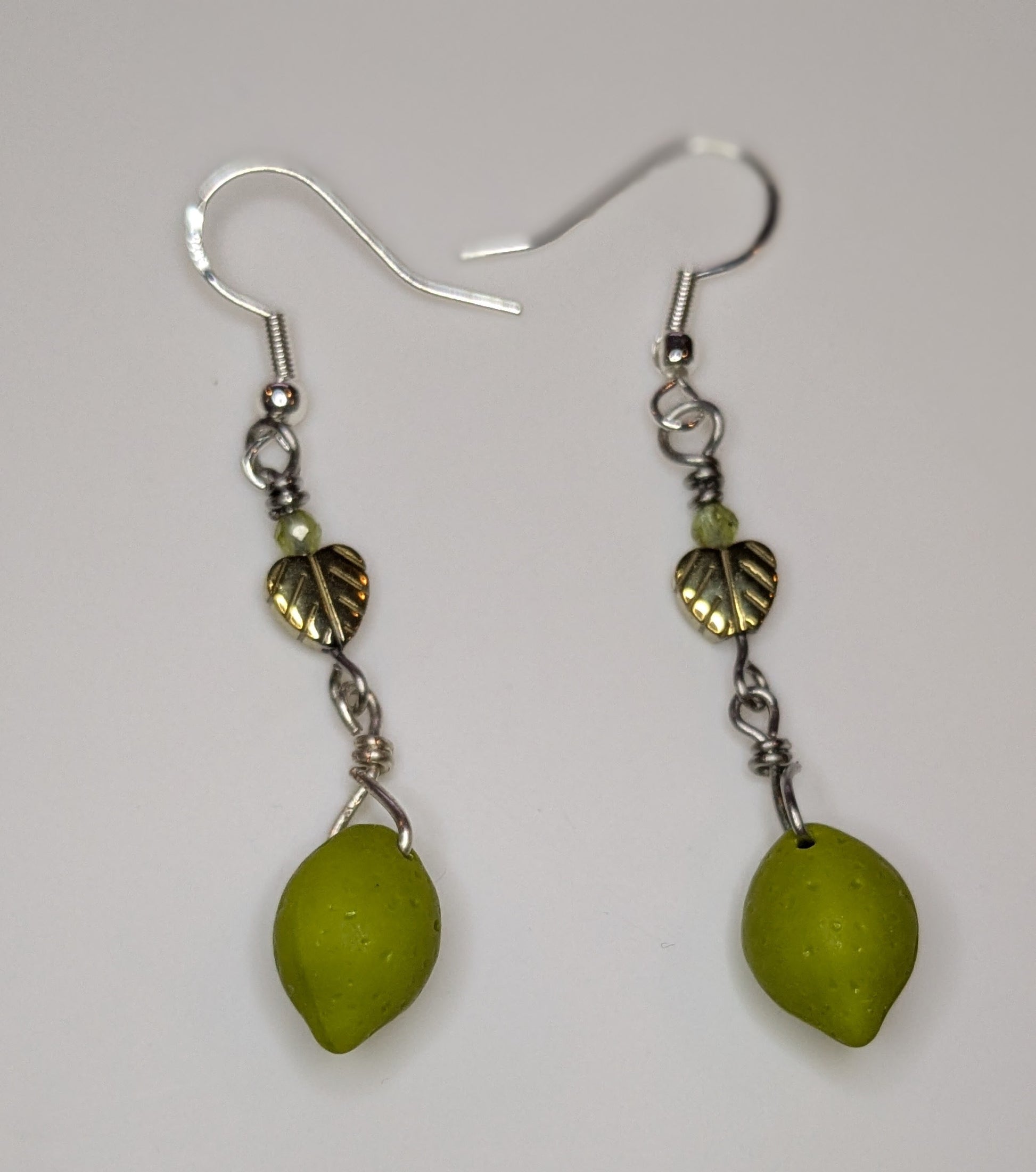 Pair of earrings with green lime shaped charms and copper leaves with peridot accents on a light gray background