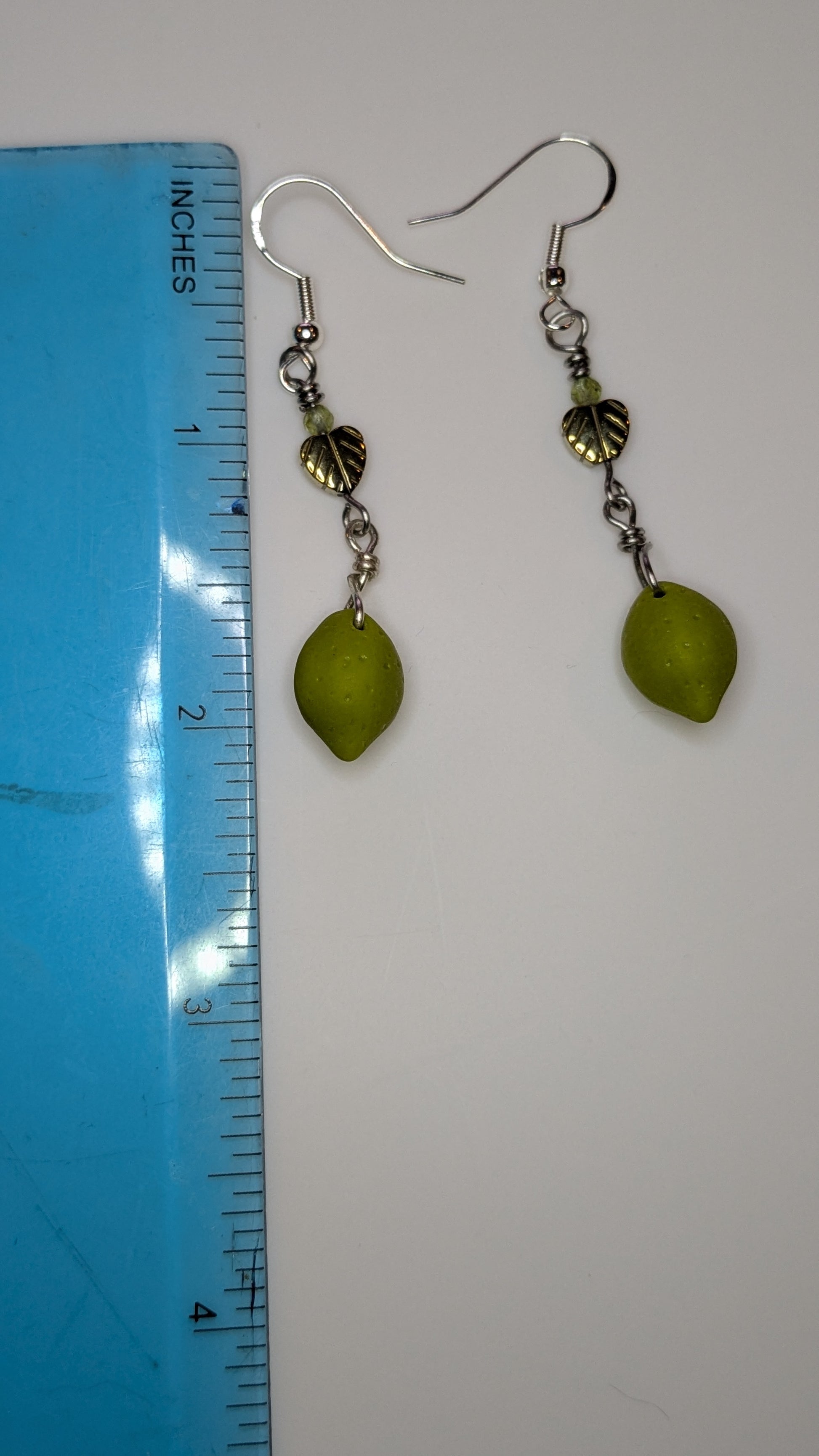 Green leaf-shaped earrings on a white background with a ruler for scale.