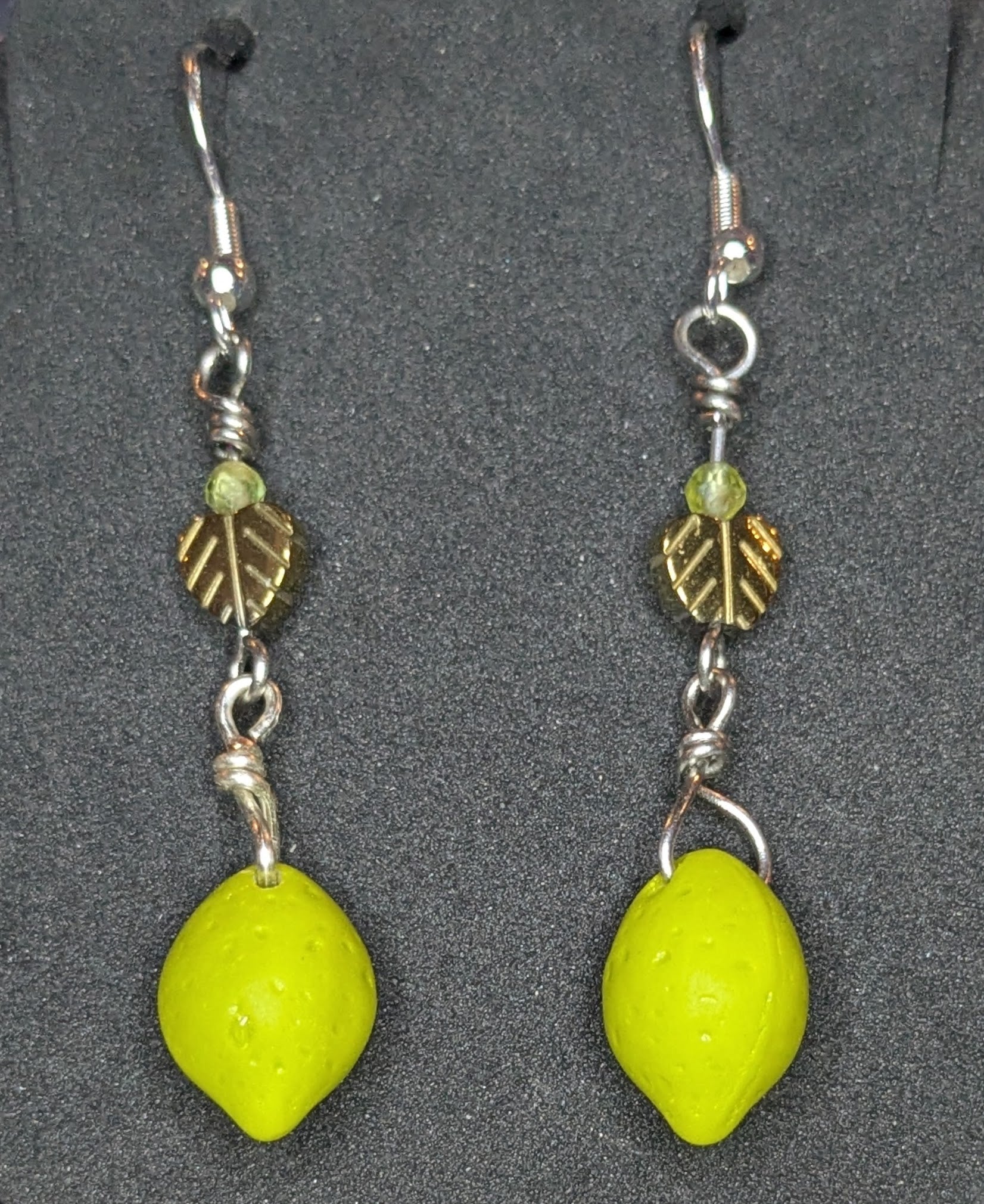 Pair of earrings with green lime shaped charms and copper leaves with peridot accents on a black earring display