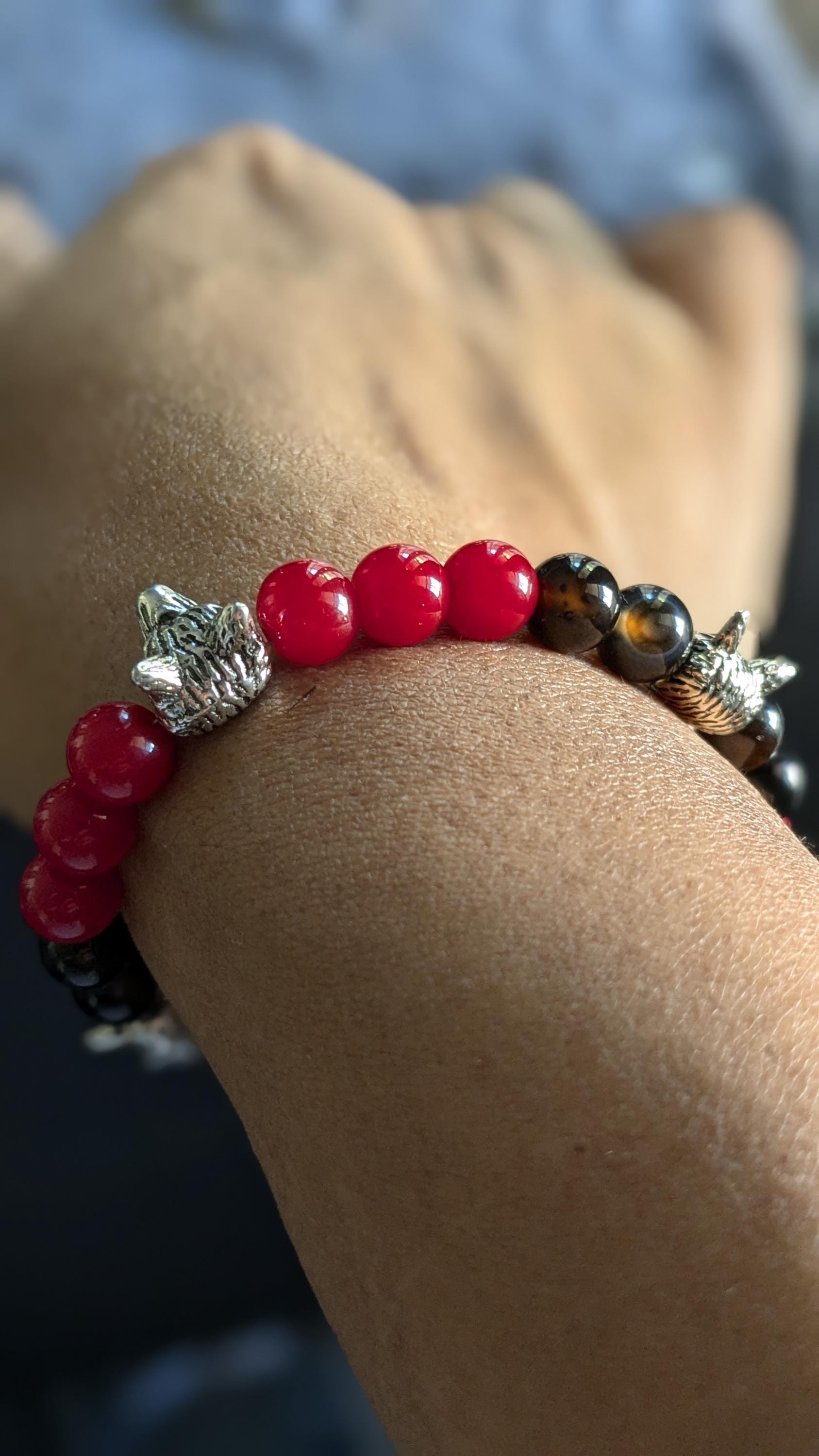 A close-up image of a person wearing a bracelet with silver wolf head shaped bead accents, black beads, and red round glass beads.