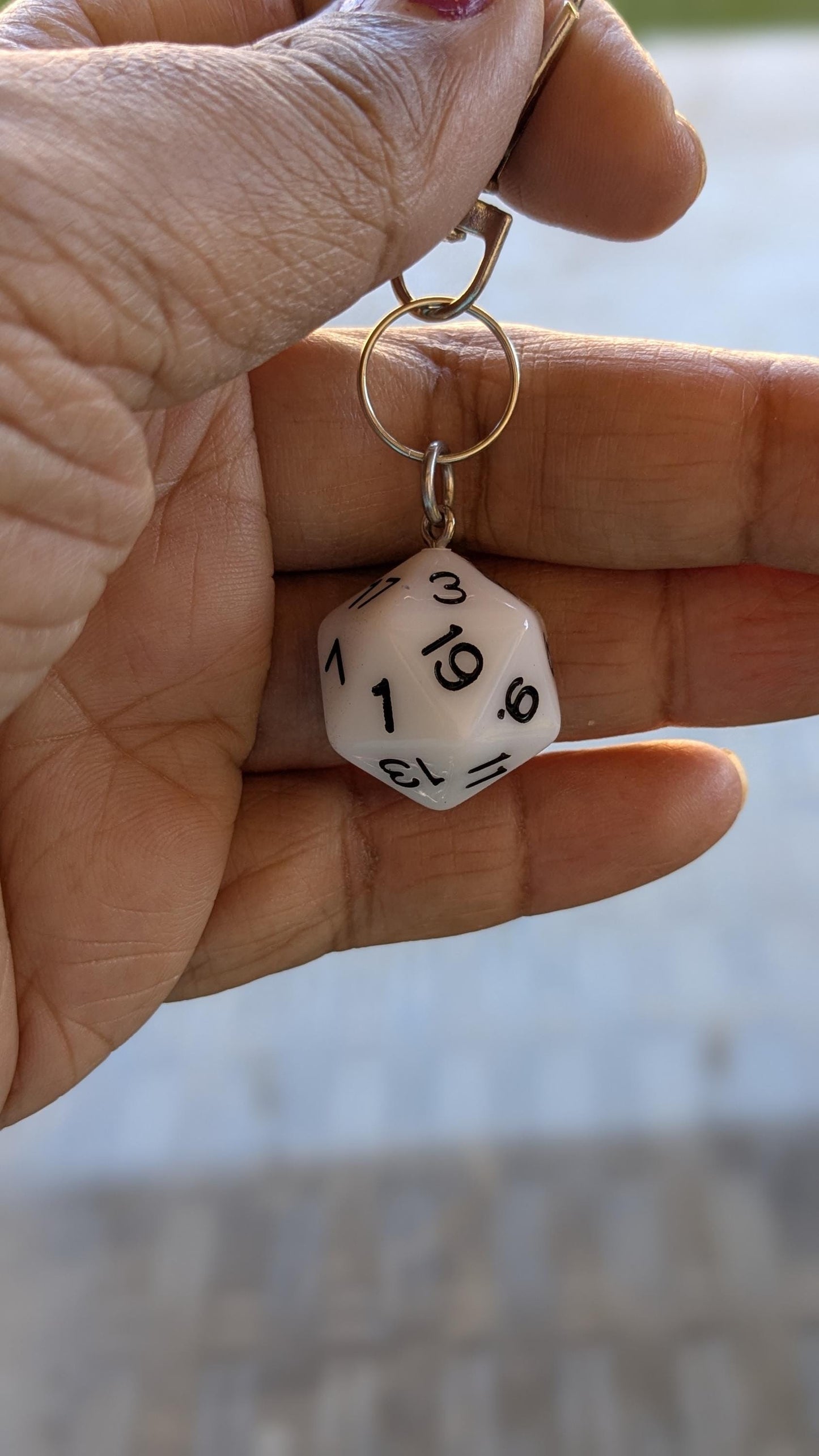 White D20 key chain dangling from a person's fingers