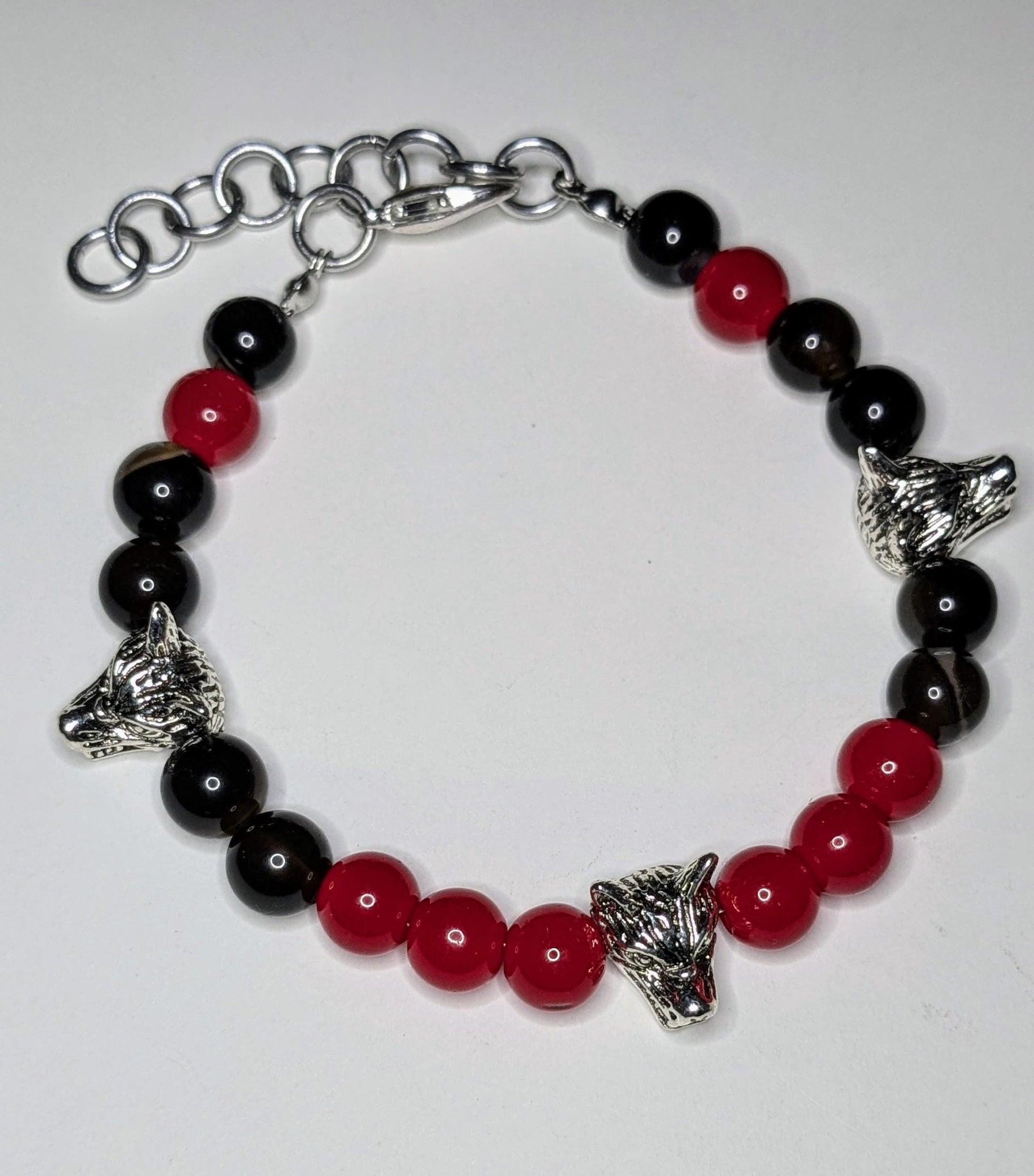 Overhead view  a bracelet with silver wolf head shaped bead accents, black and red round glass beads.  The bracelet has a lobster clasp and an extender chain