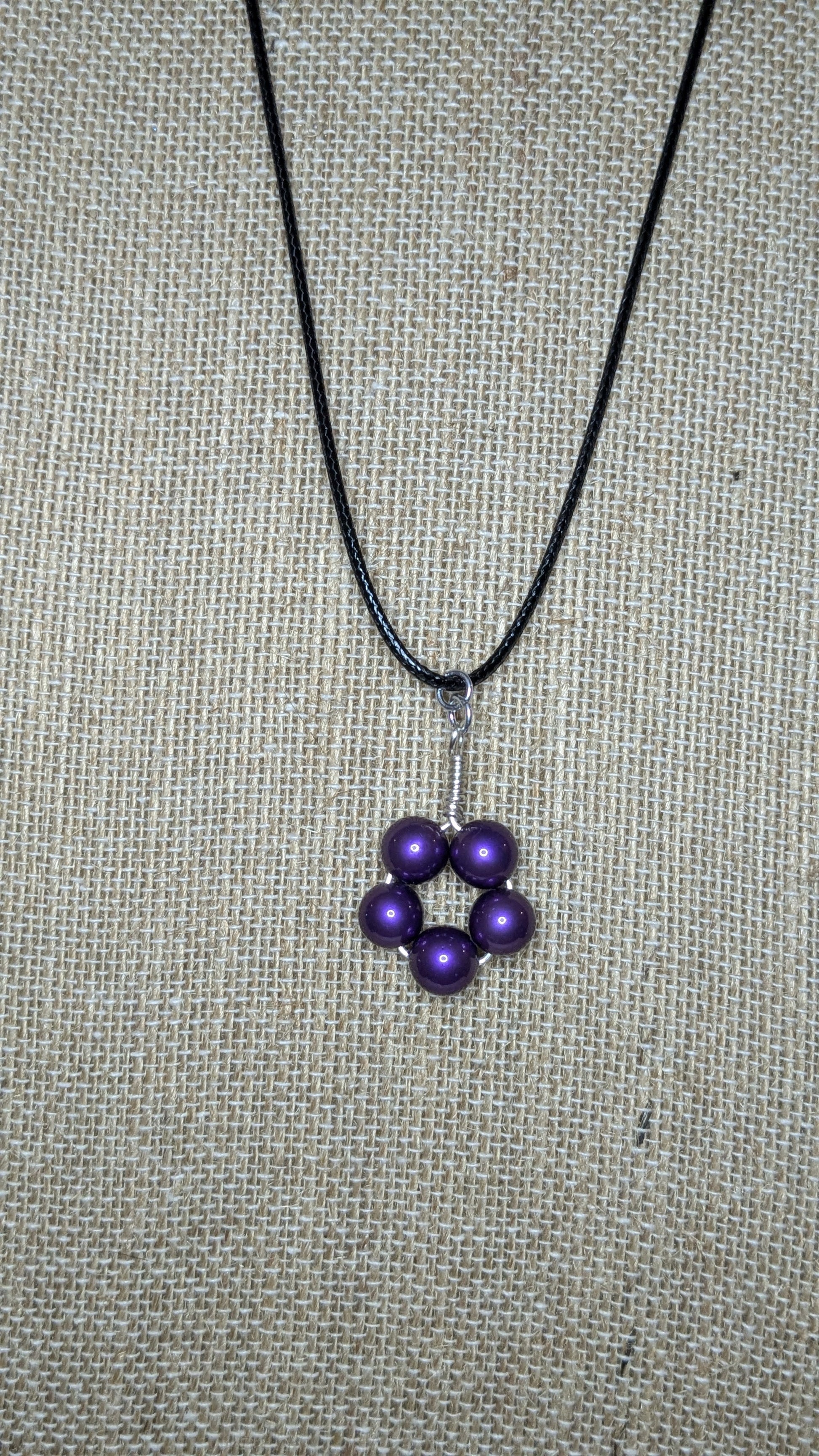 A pendant with purple glass pearls wire wrapped into a circle on a black cord