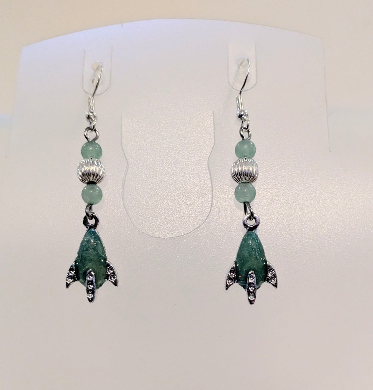 Green beaded earrings with enameled retro spaceship charms on a white background