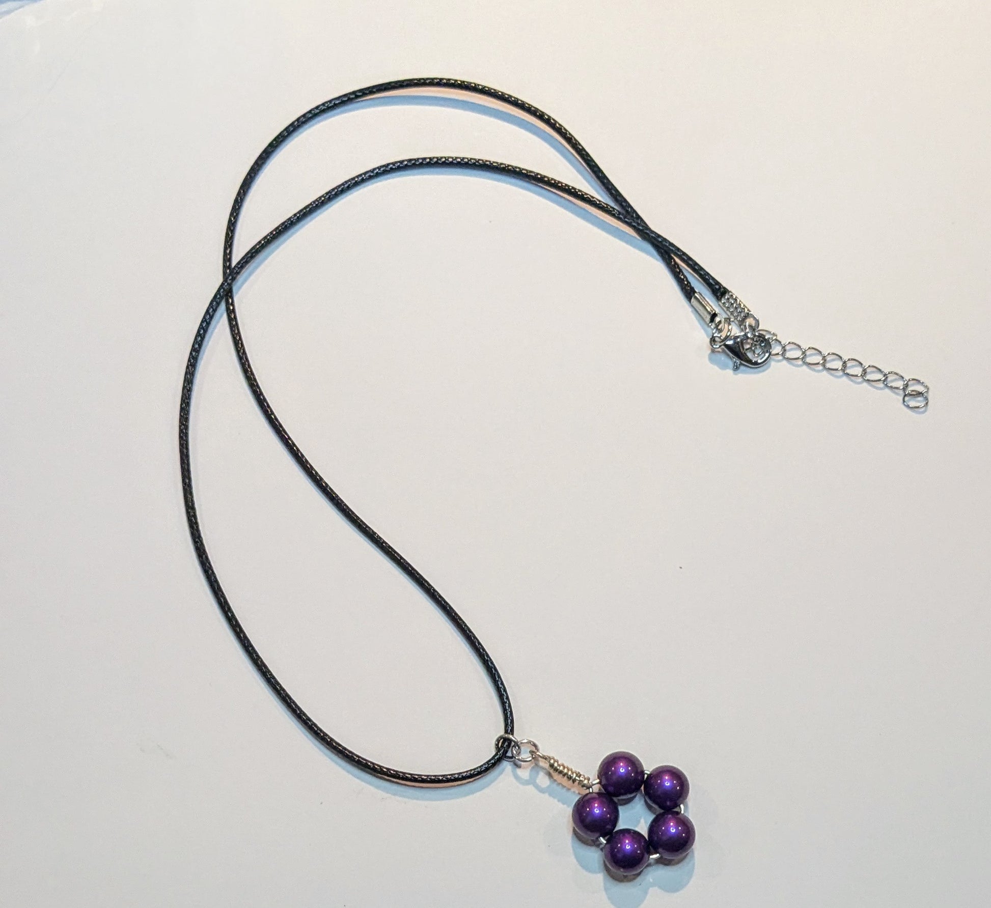 A pendant with purple glass pearls wire wrapped into a circle on a black cord