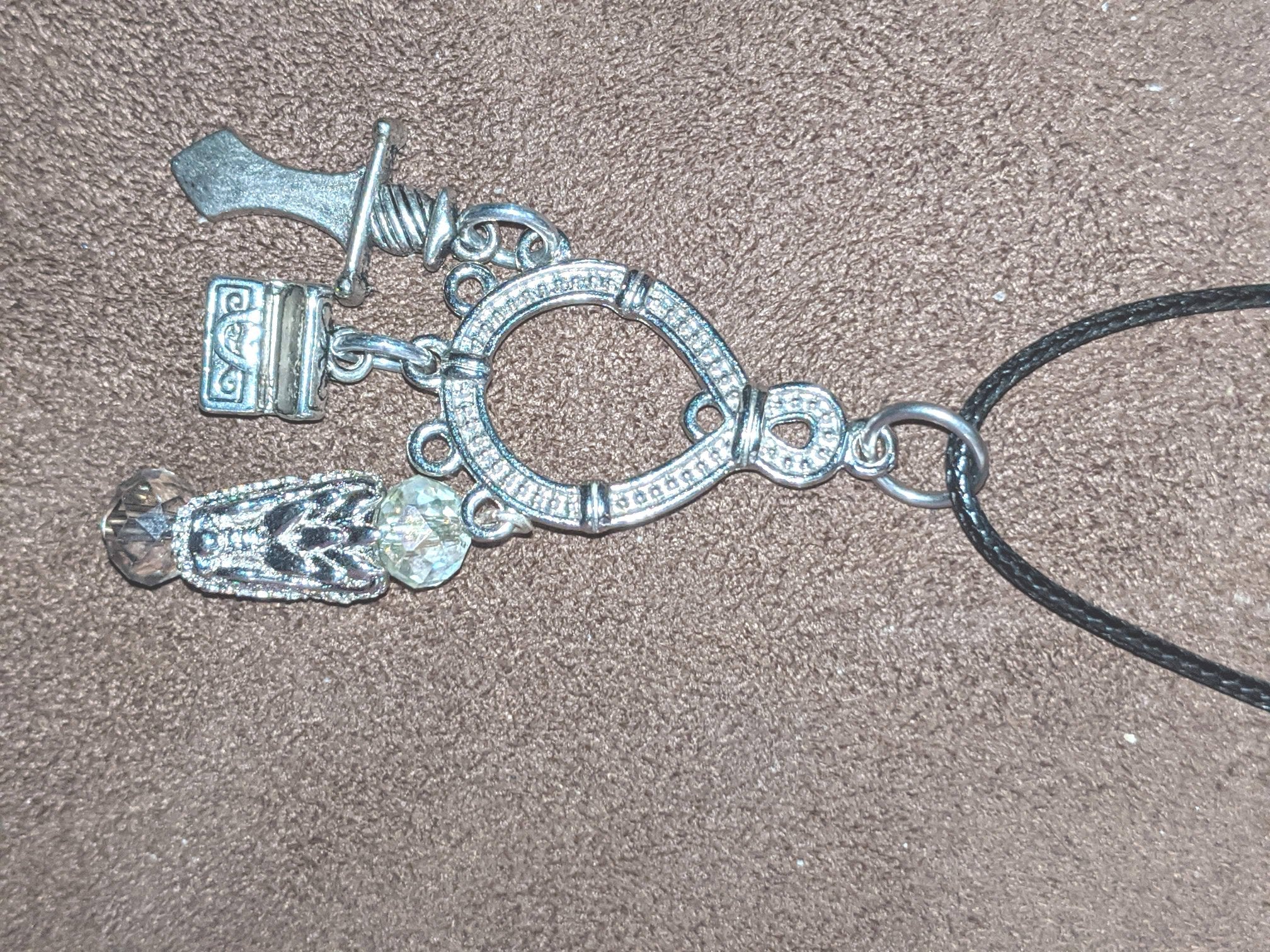 A silver-colored metal pendant featuring a dragon design, attached to a black cord necklace.