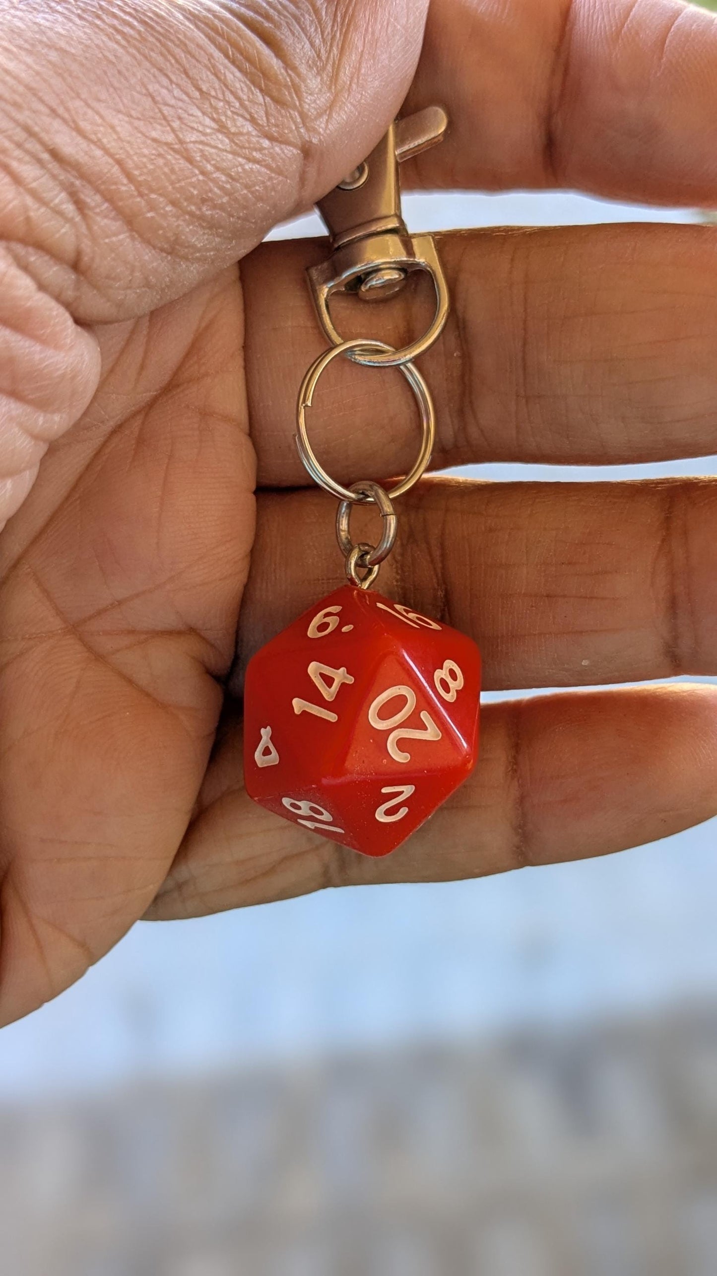 Red D20 key chain dangling from a person's fingers
