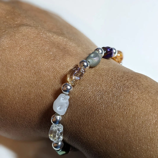 Colorful acrylic skull and silver colored metal beaded bracelet on a brown person's wrist 