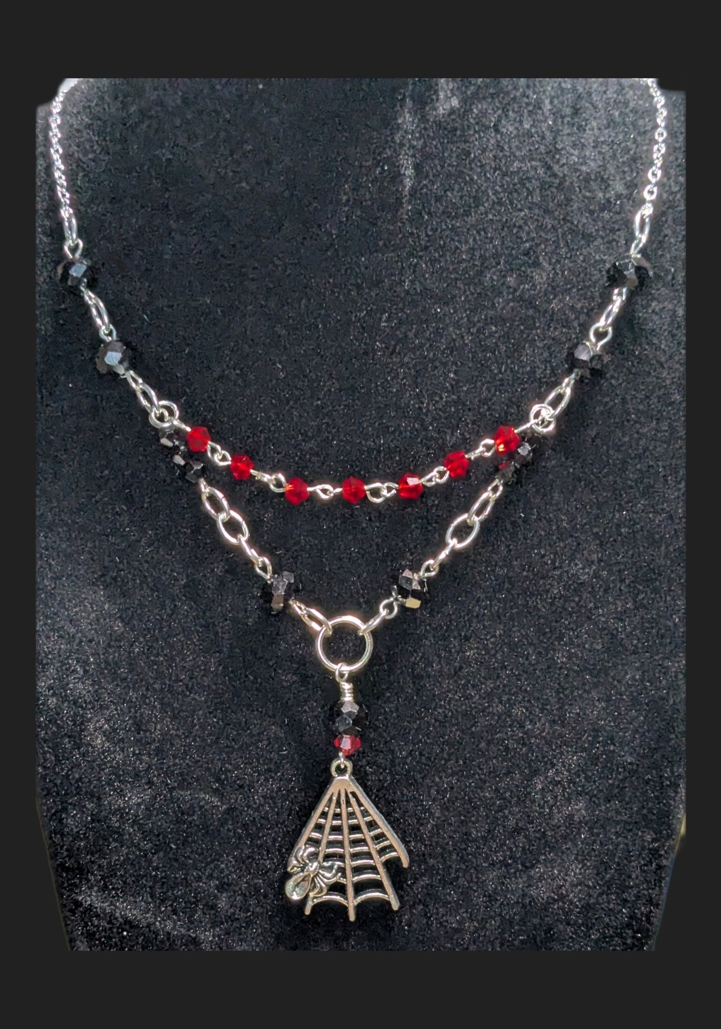 Necklace with spider web pendant and red beads on a dark background