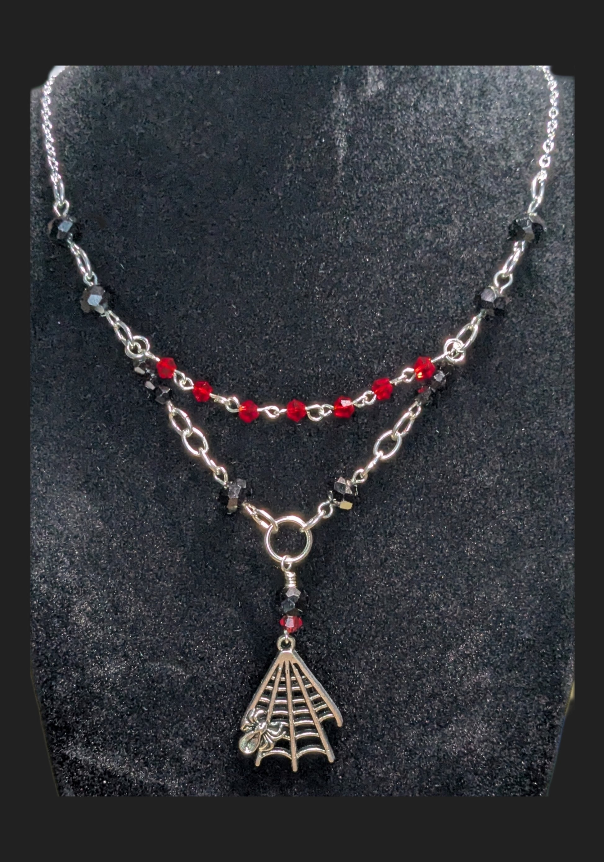 Necklace with spider web pendant and red beads on a dark background