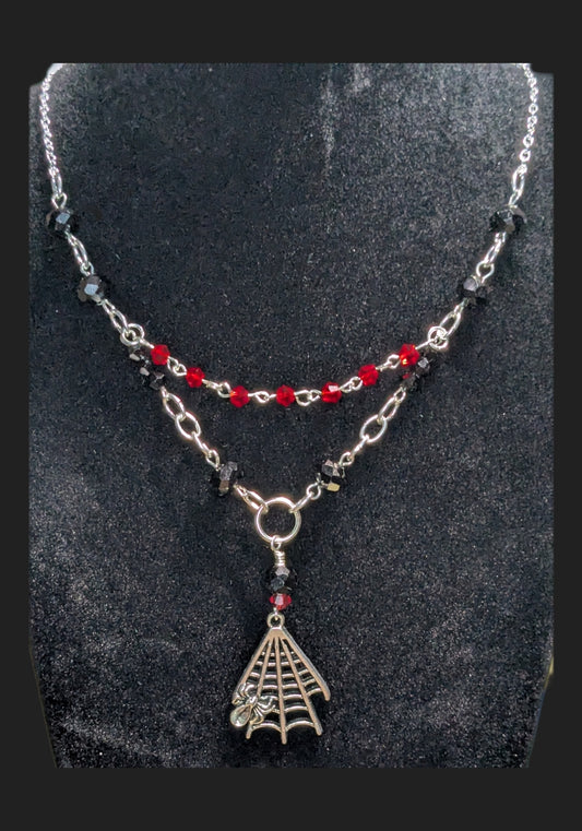 Necklace with spider web pendant and red beads on a dark background