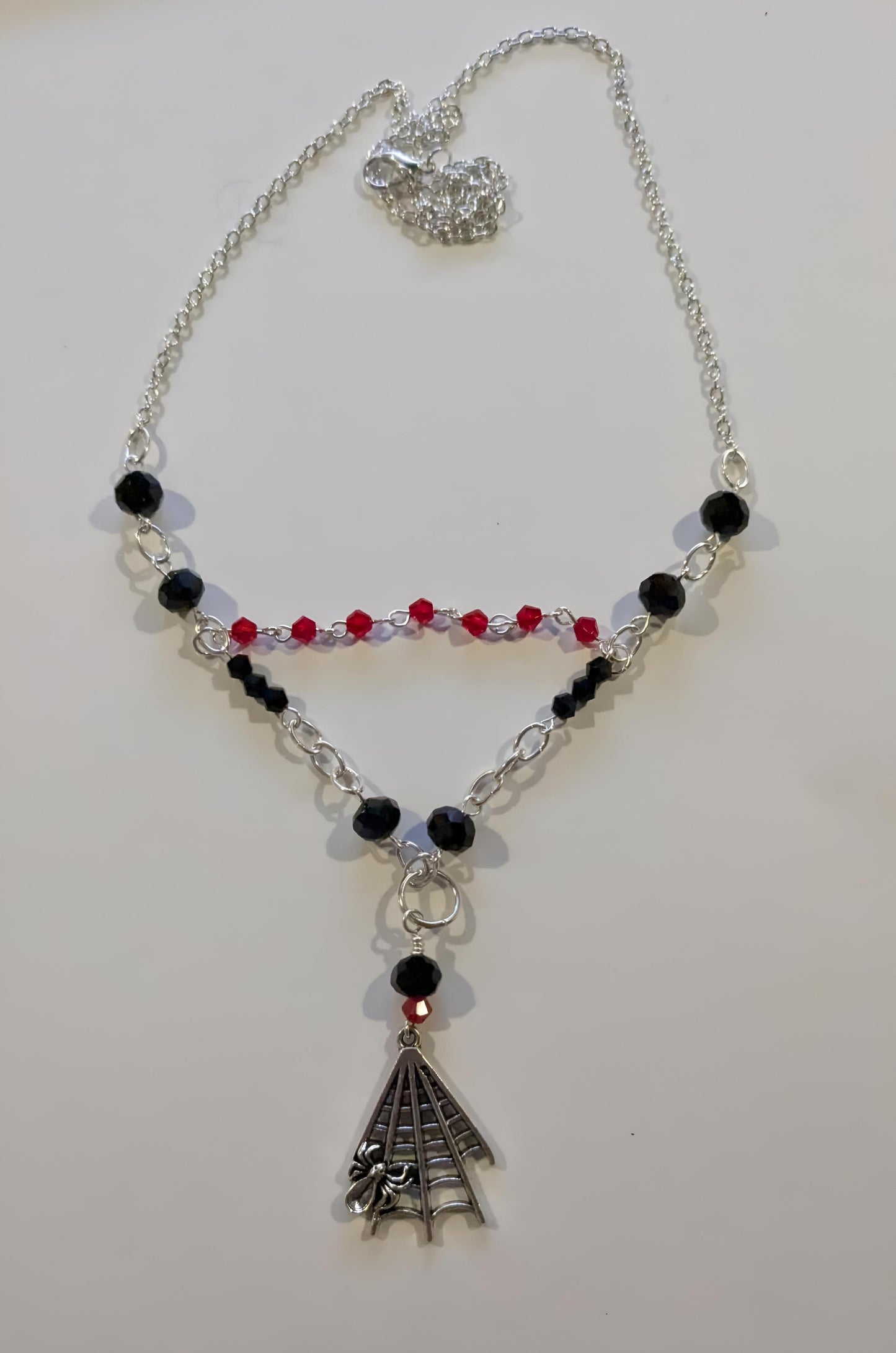 Necklace with black and red beads and a silver spiderweb pendant on a white background