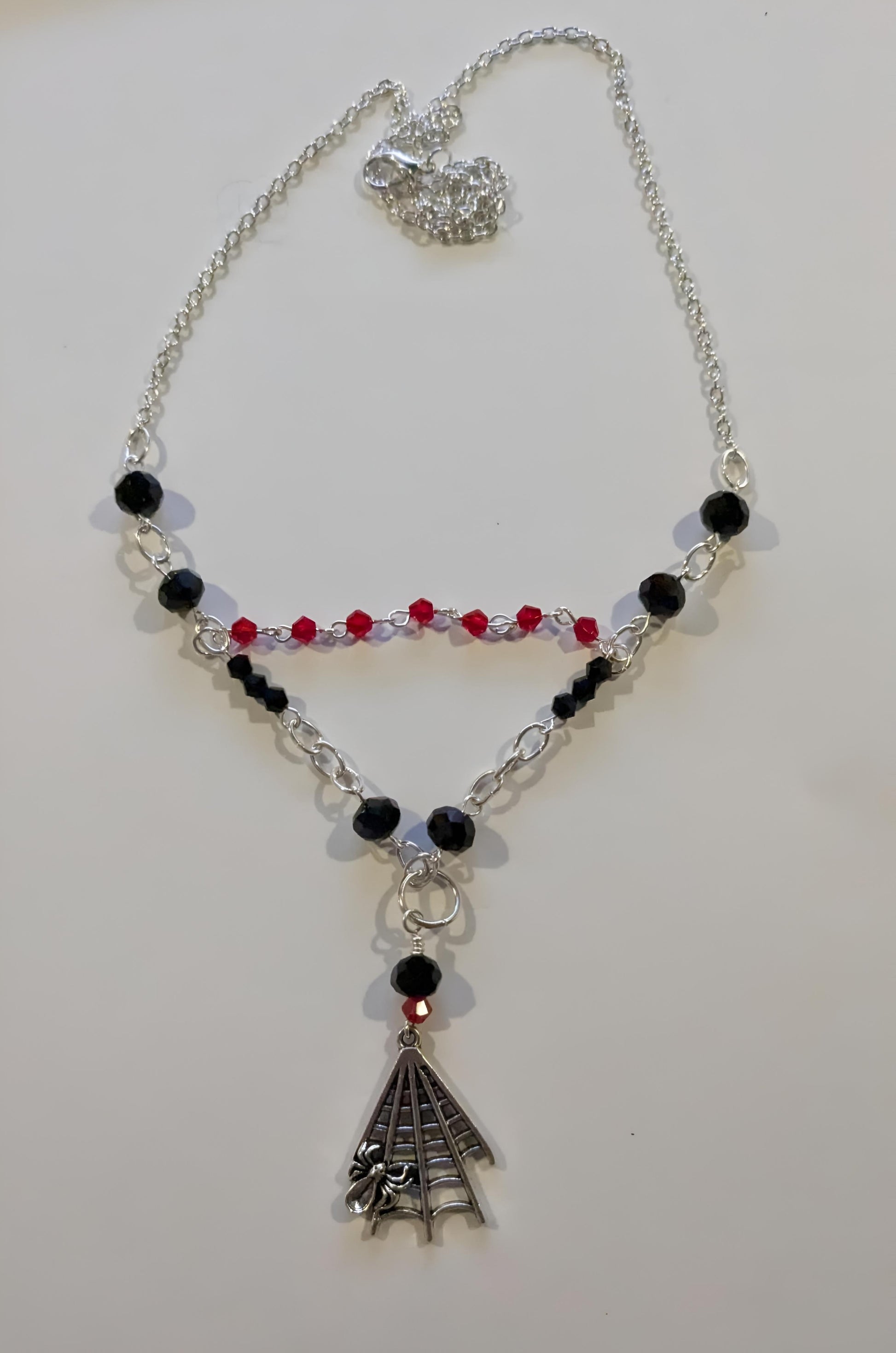 Necklace with black and red beads and a silver spiderweb pendant on a white background